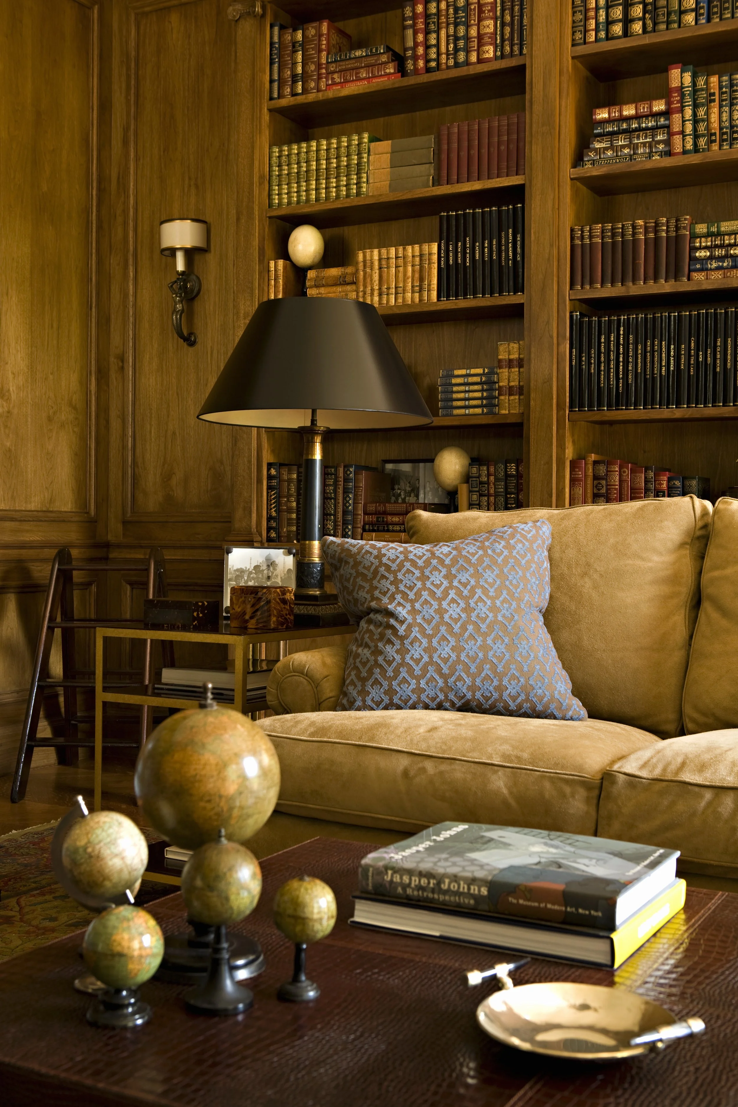 Library corner with a tan sofa, blue patterned pillow and built-in bookshelves