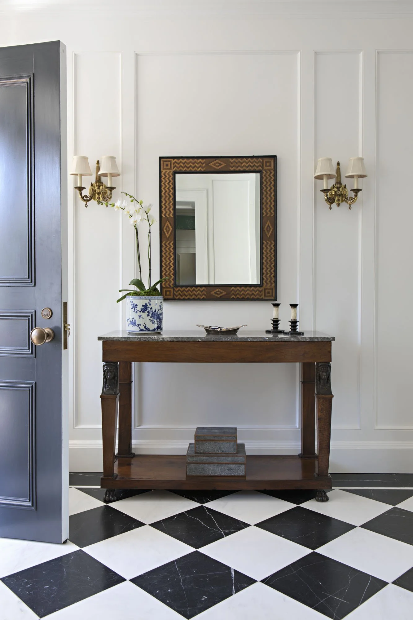 Entry with a slate blue door, walnut console, framed mirror and brass sconces
