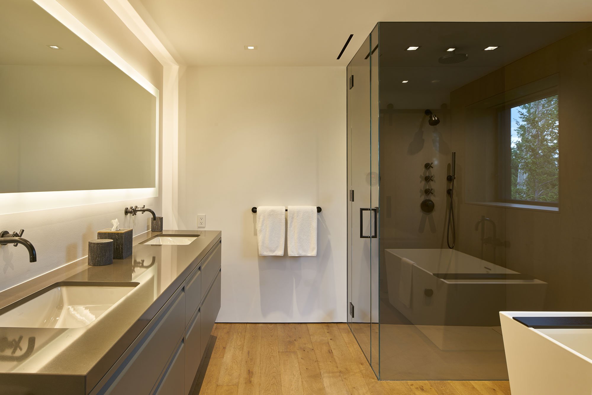Bath with a long floating vanity, backlit mirror and glass shower