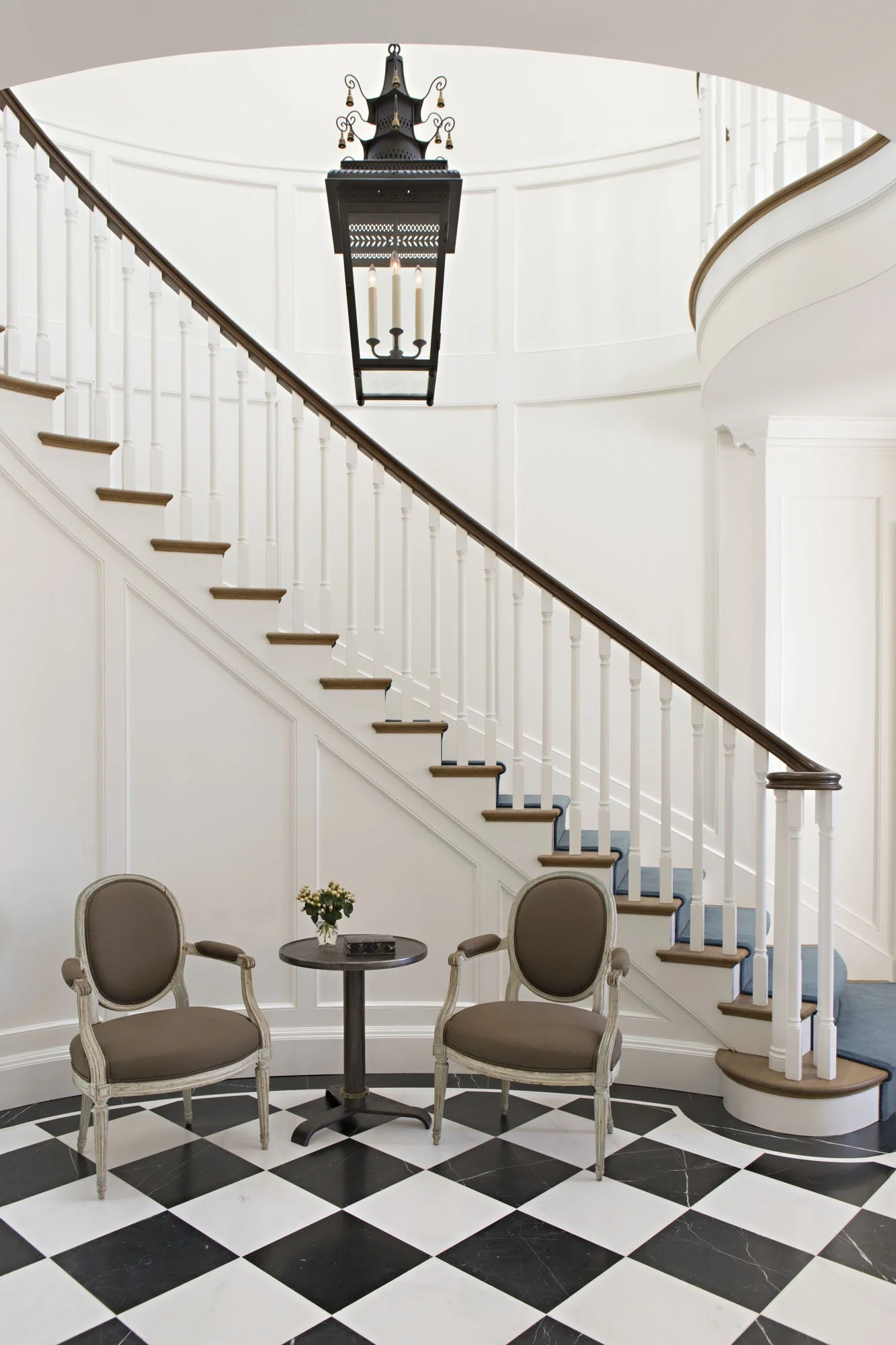 Curved staircase with white balustrade and wood handrail, and two upholstered chairs at a small table