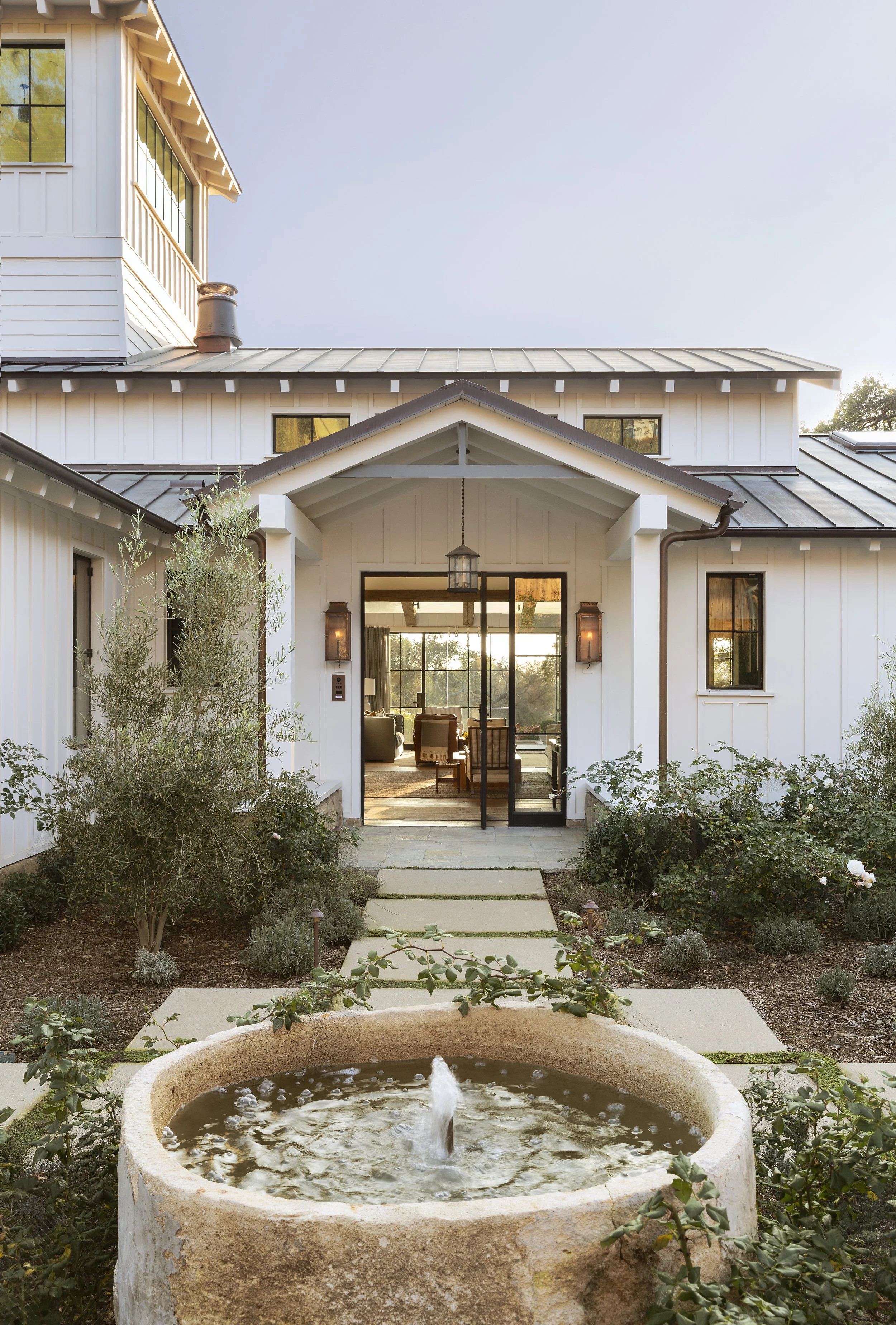 White board and batten farmhouse with a gabled entry porch, steel-framed doors and lanterns