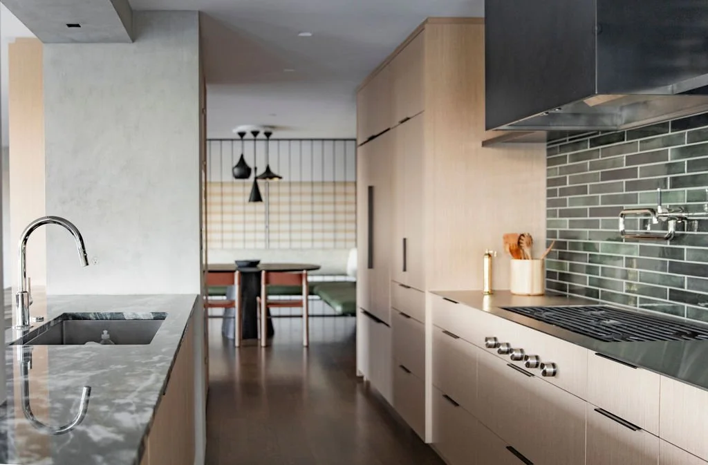 Kitchen with pale oak cabinetry, stone counters and a green tile backsplash