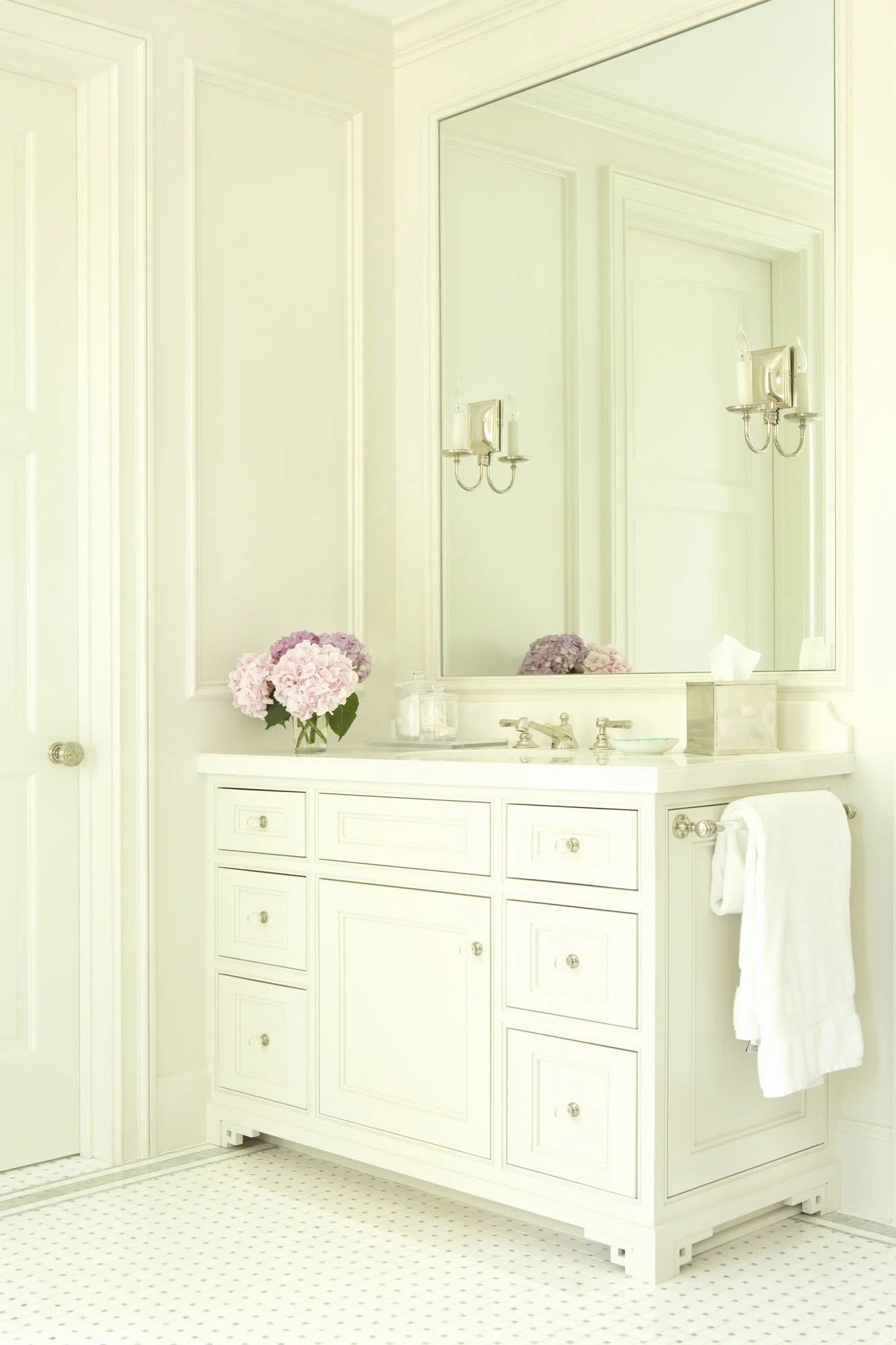 White bathroom vanity with fresh hydrangeas, nickel sconces and mirrored wall