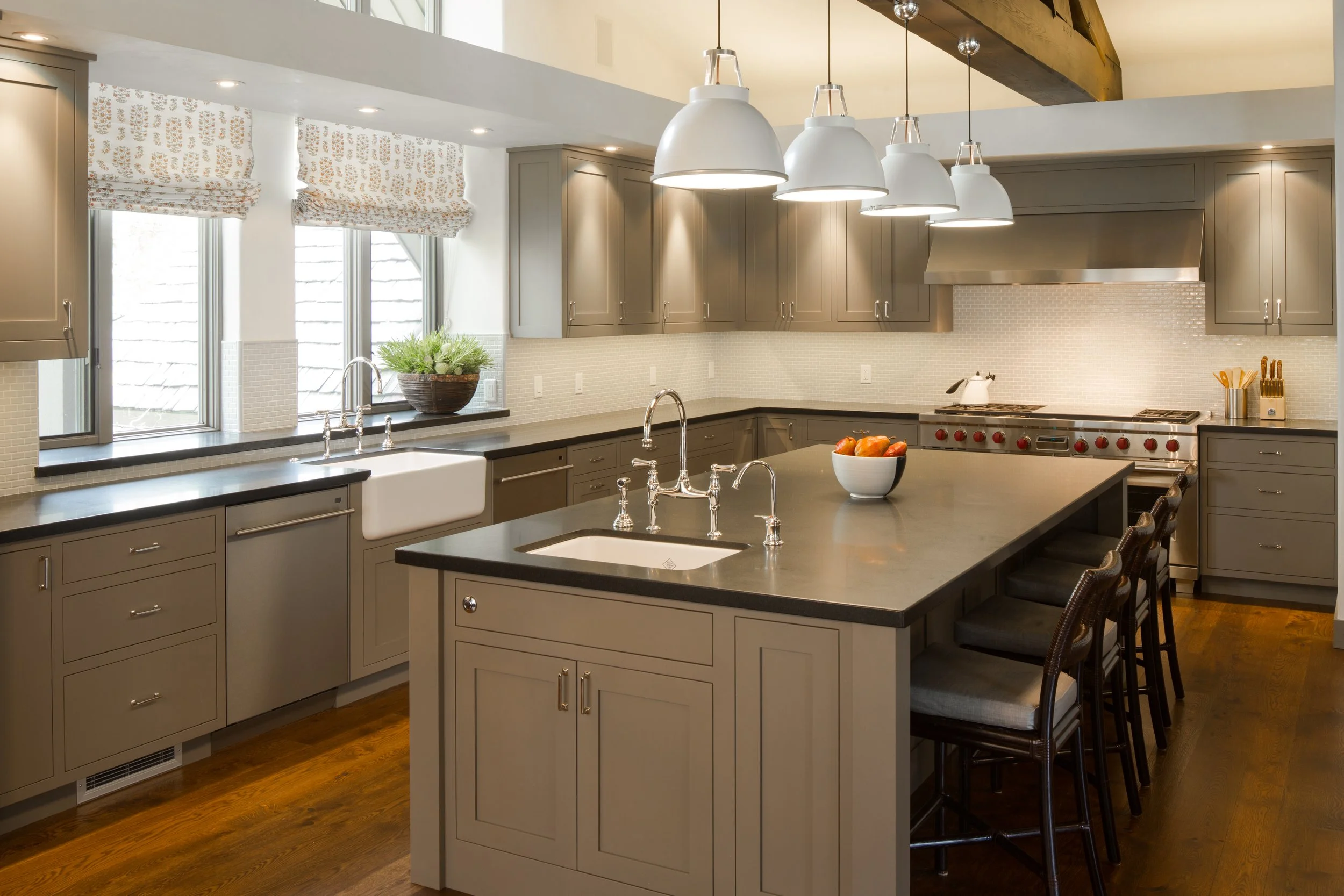 Kitchen with gray cabinetry, a dark island with counter stools, white pendant lights and a farmhouse sink