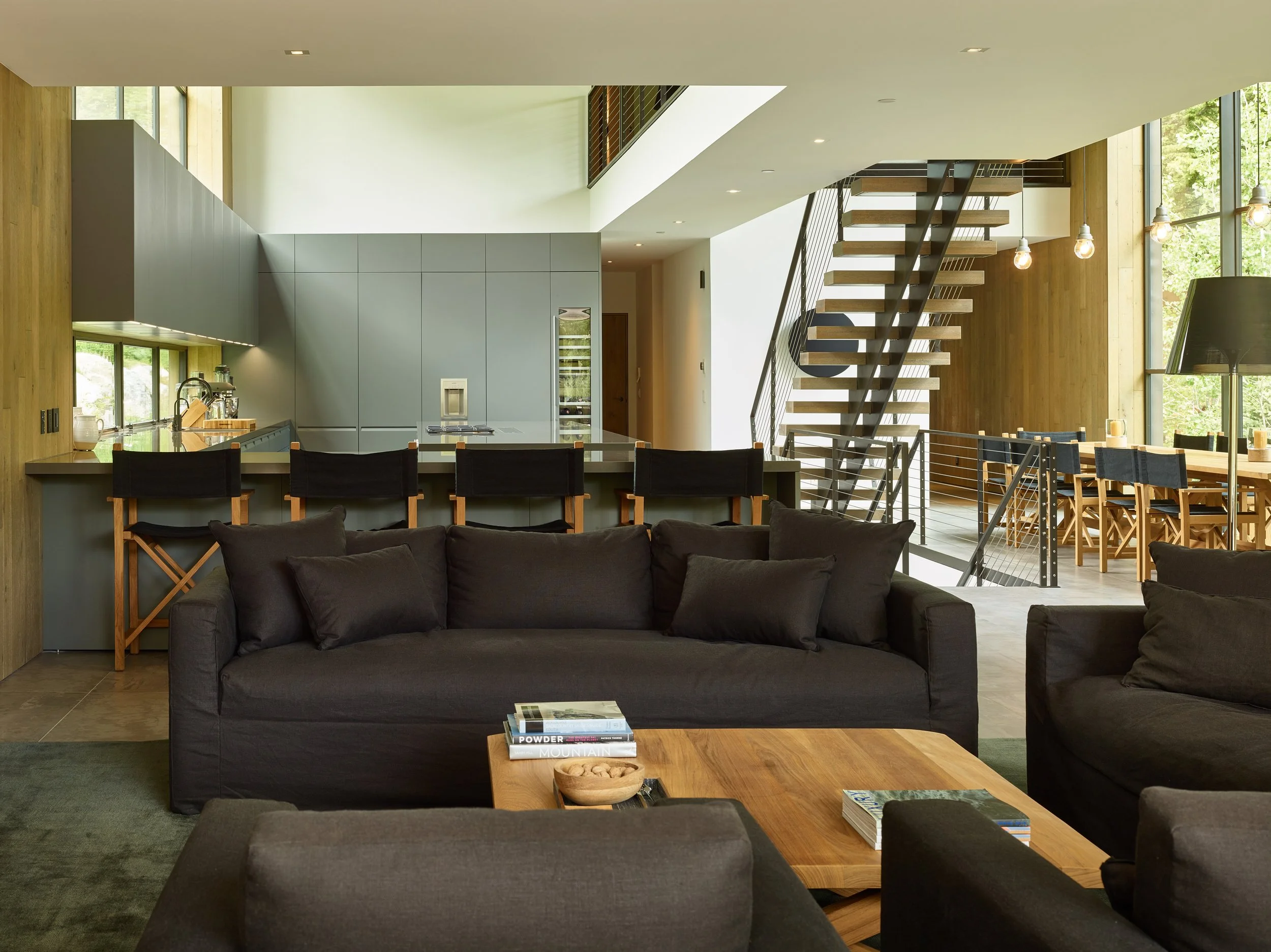 Living area with a charcoal sofa, open kitchen and floating stairs in a double-height room