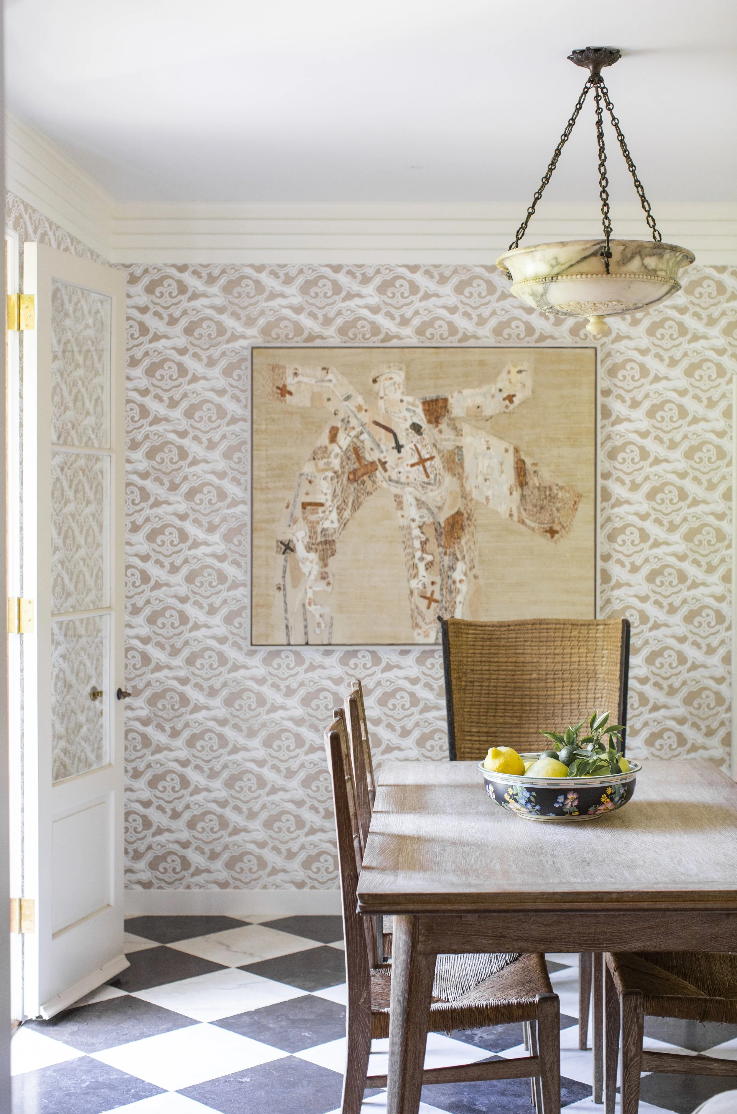 Breakfast nook with a wood table and cane-seat chairs, patterned wallpaper, an abstract painting and a black-and-white checkered floor