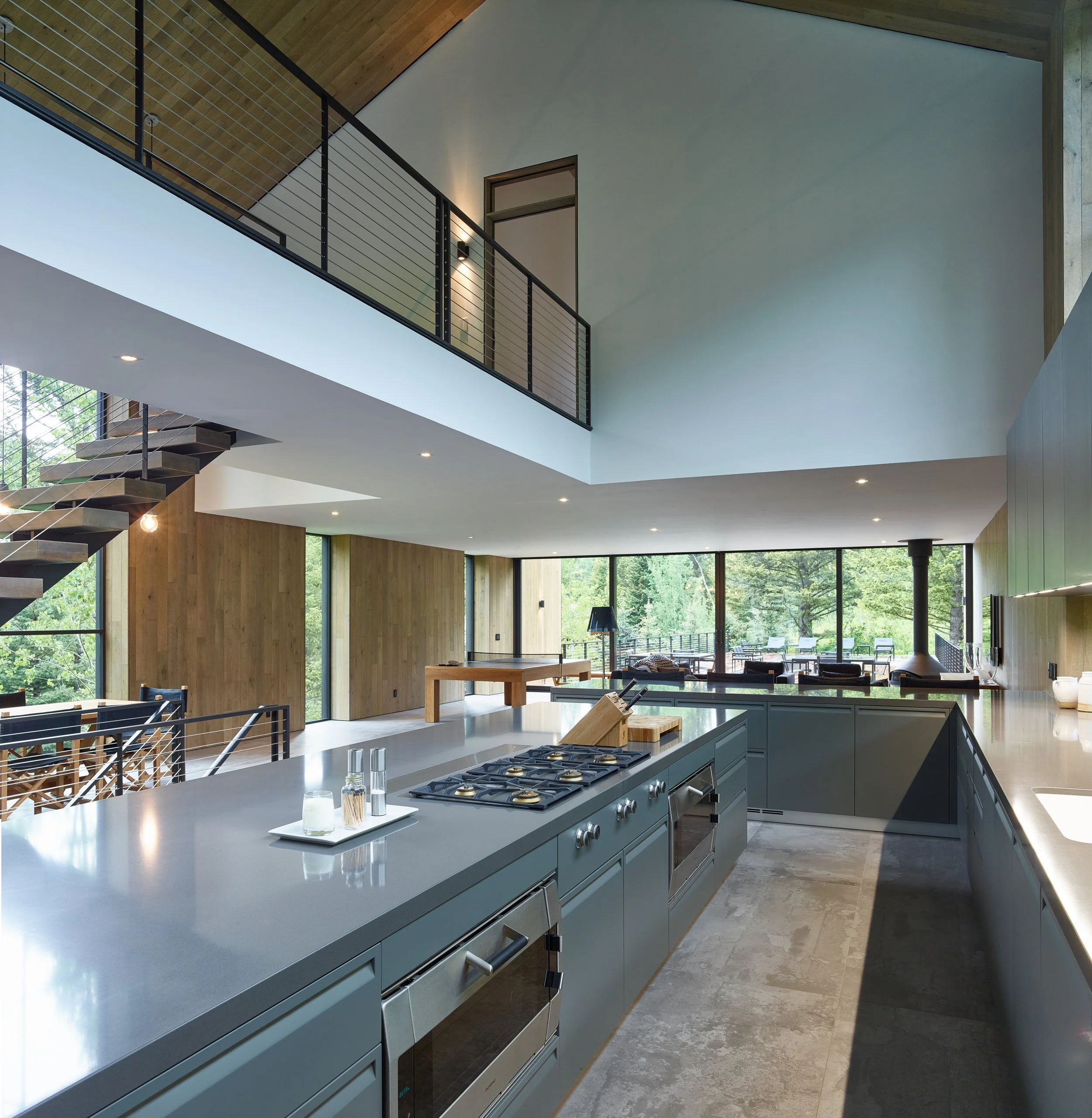 Kitchen island with a gas cooktop beneath a mezzanine, with forest views