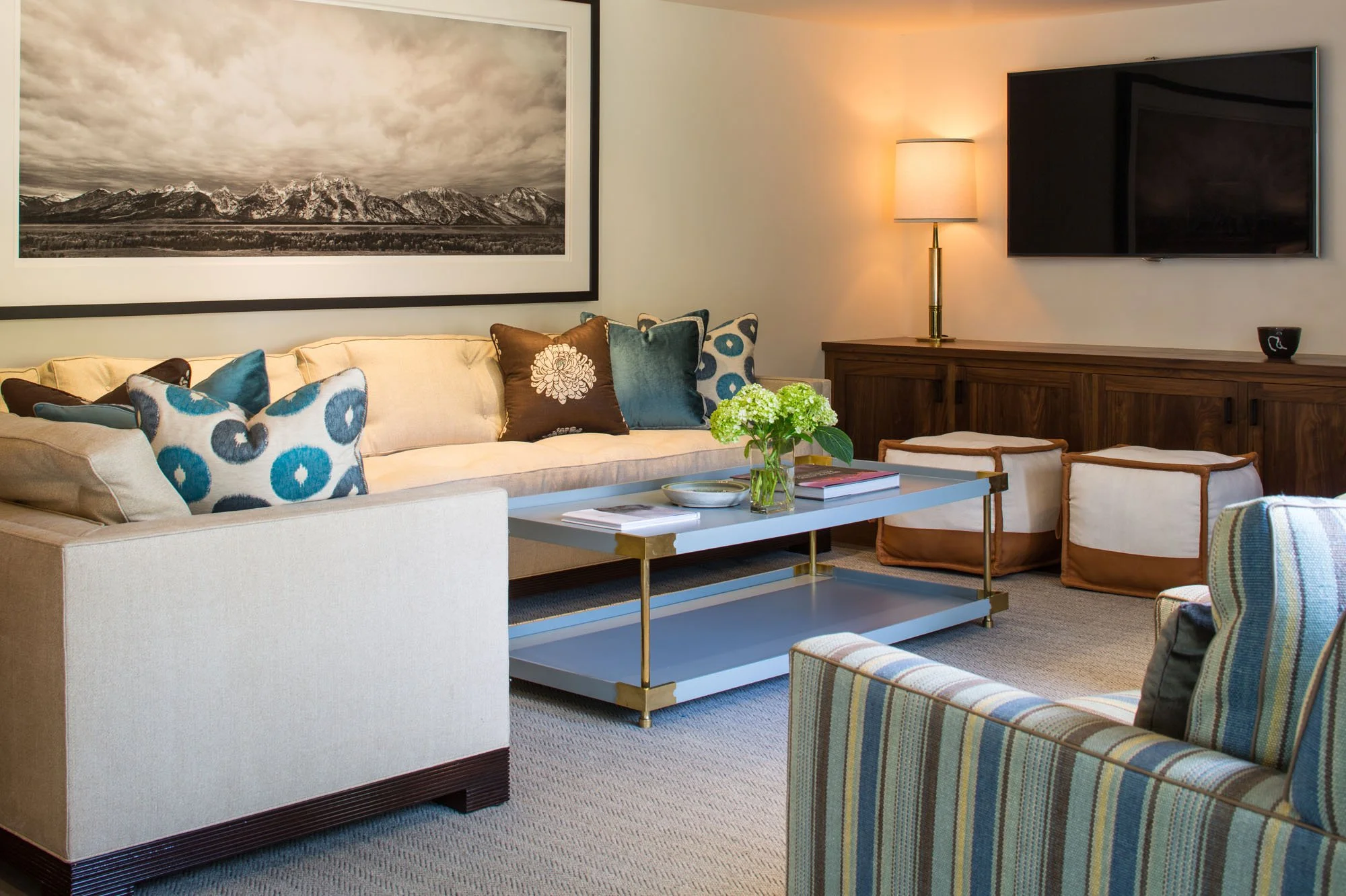Sitting room with a framed mountain panorama, a blue lacquered coffee table, patterned pillows and a striped chair