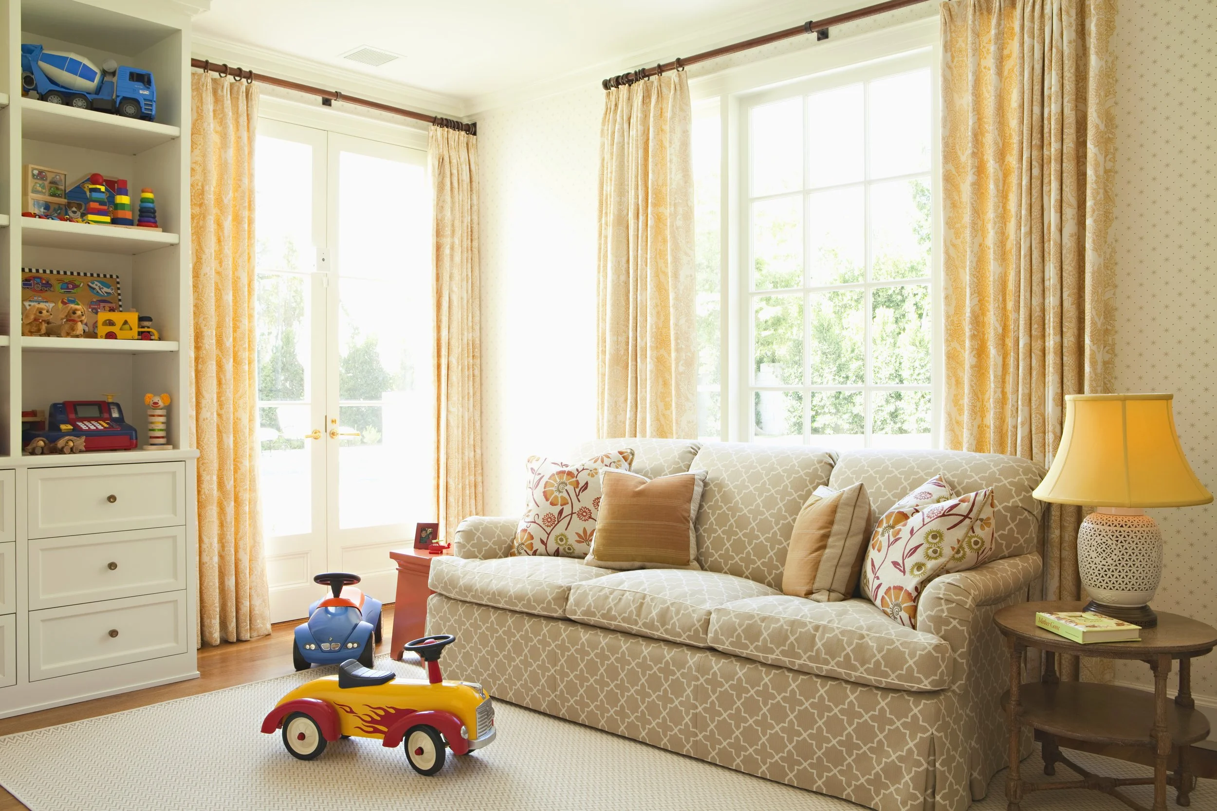 Playroom with a quilted sofa, built-in toy shelves and yellow drapes