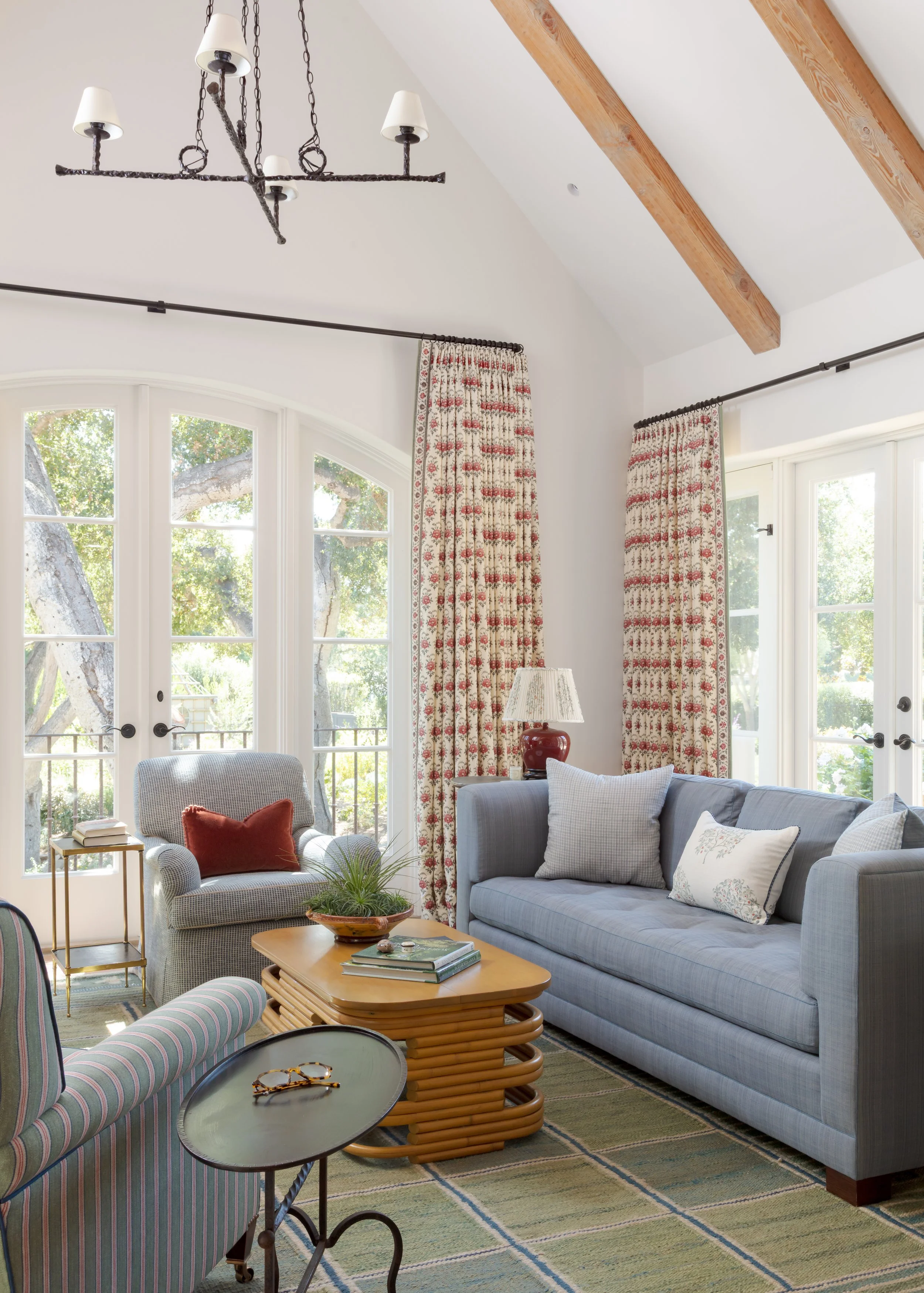 Living room with arched French doors, red and cream floral curtains, a blue-gray sofa and a gray armchair