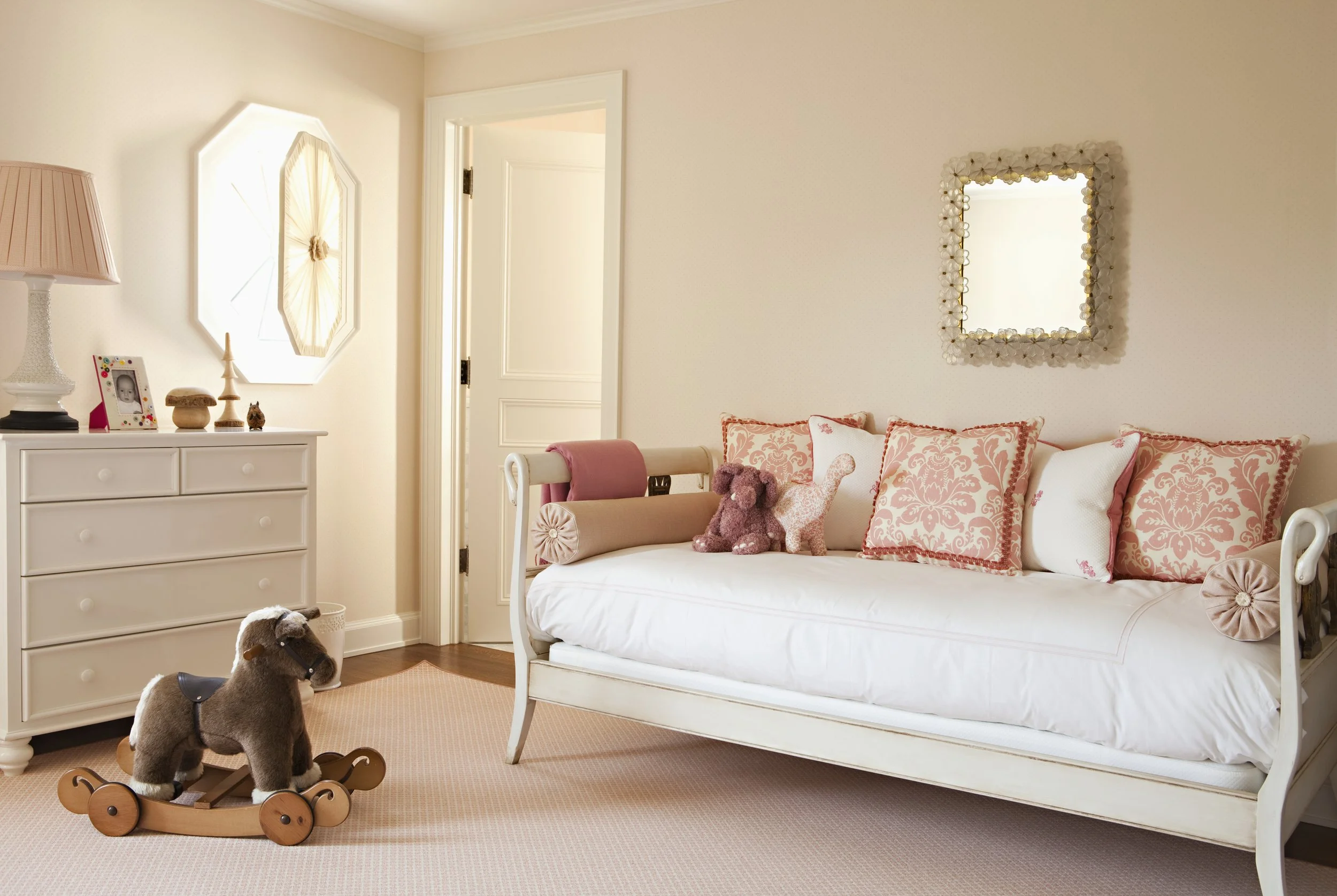 Girl's room with a white daybed, rocking horse and coral pillows
