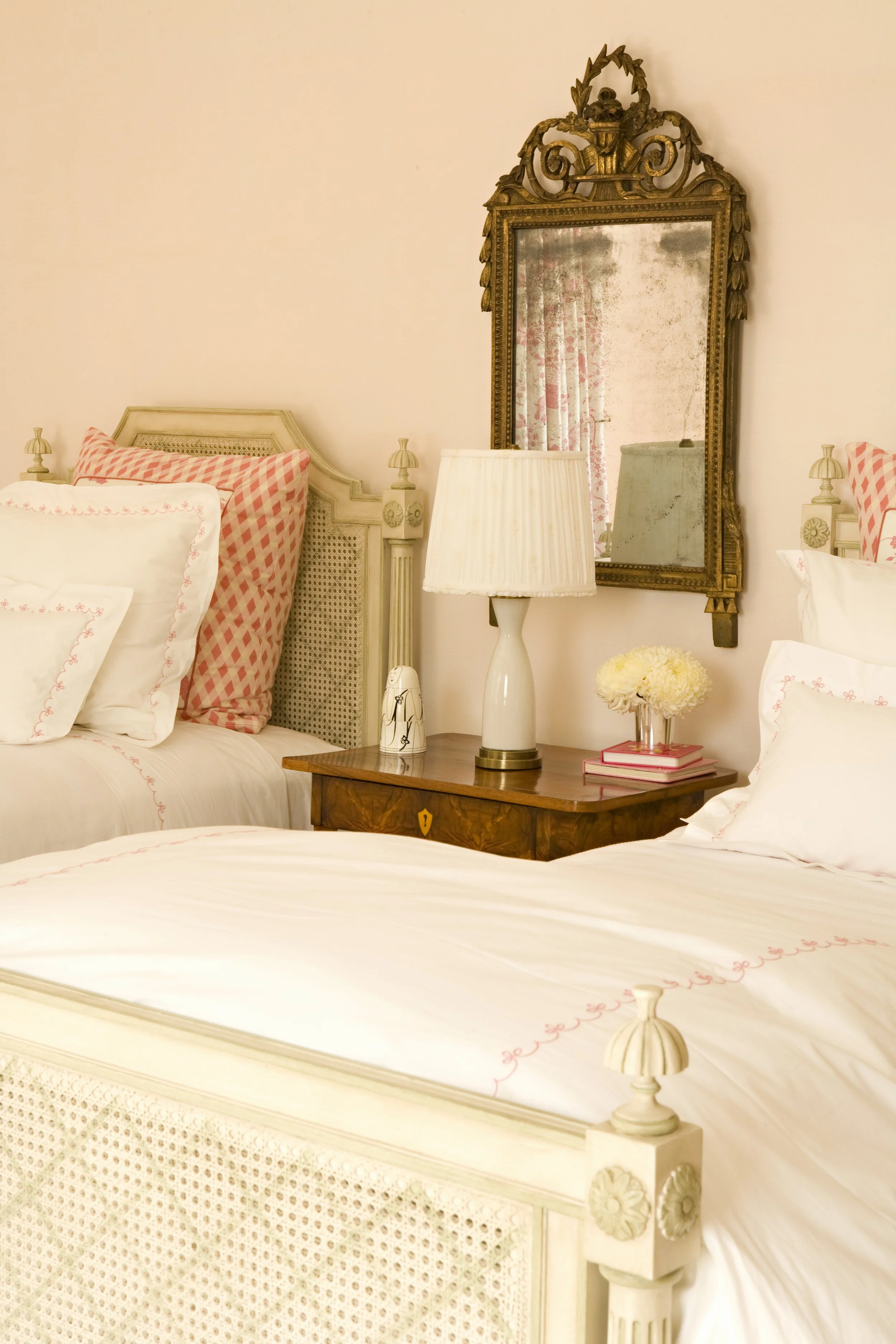 Guest bedside with a carved mirror, antique nightstand and coral pillows