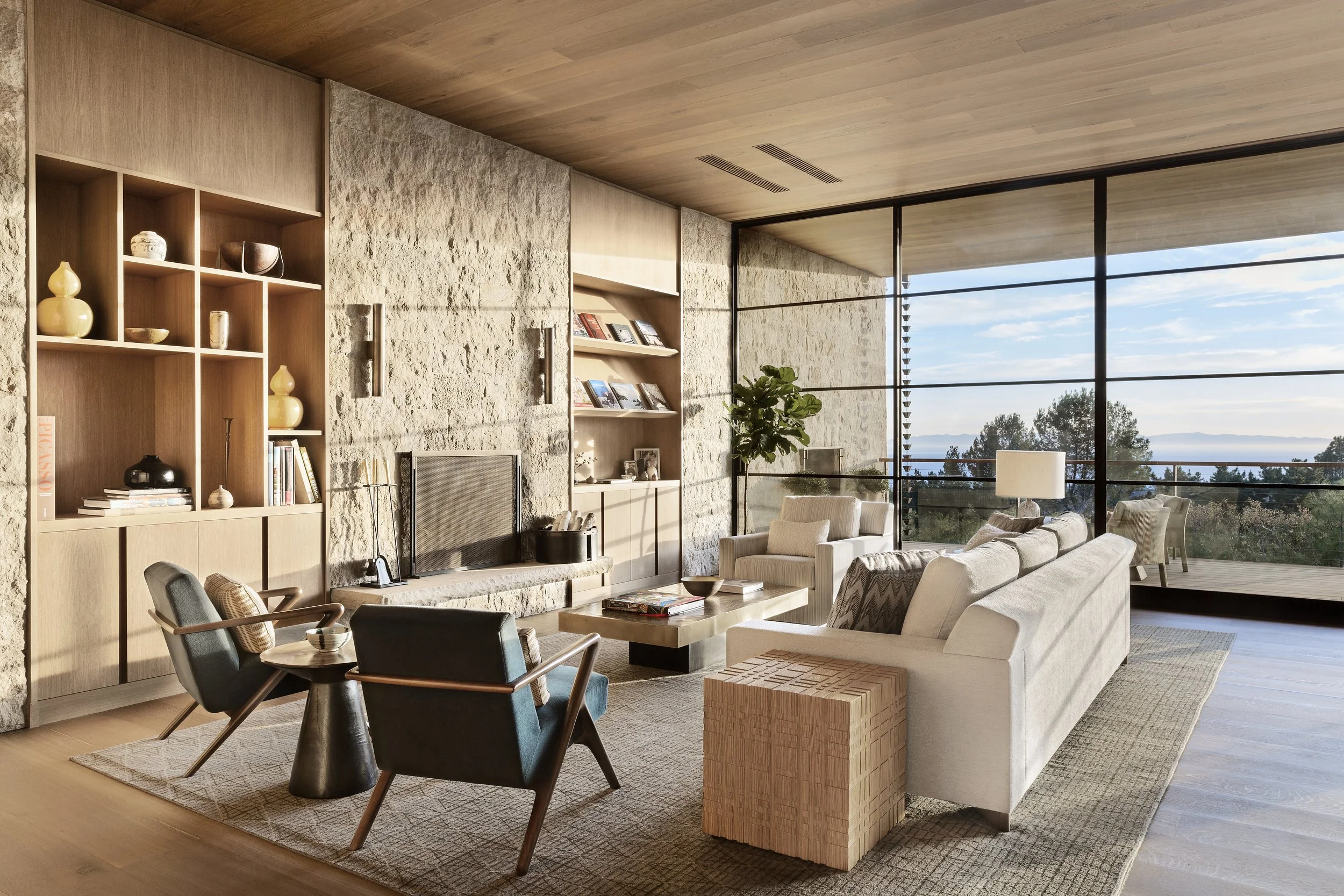 Living room with a stone wall, built-in shelves and floor to ceiling glass overlooking the valley