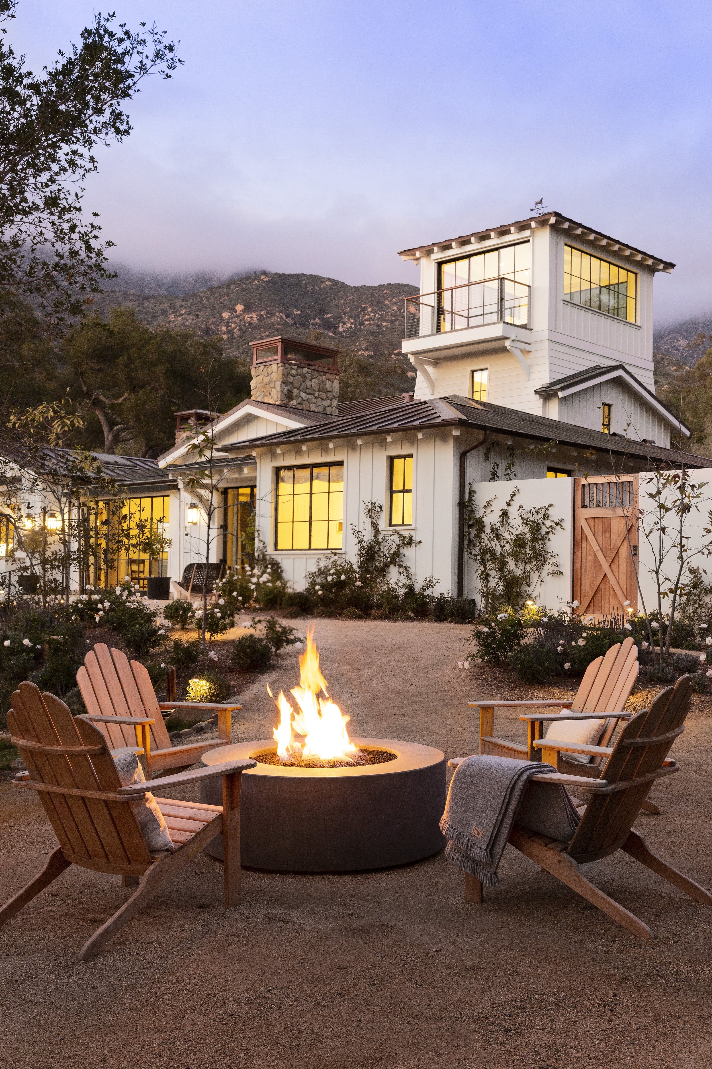 Evening courtyard with a fire pit, Adirondack chairs and a lit farmhouse with barn doors