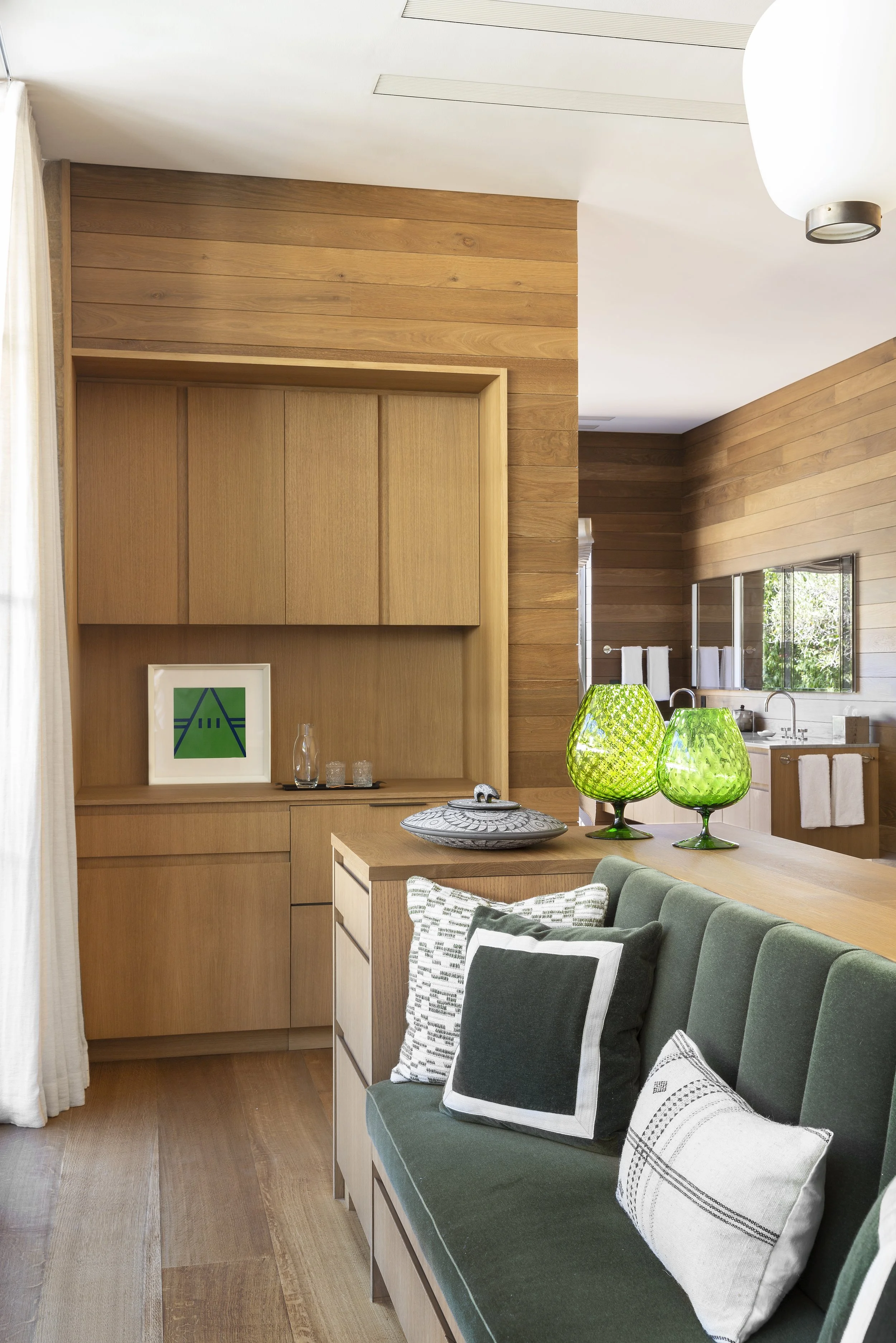 Oak built-in cabinetry with green glass vases and a green tufted sofa