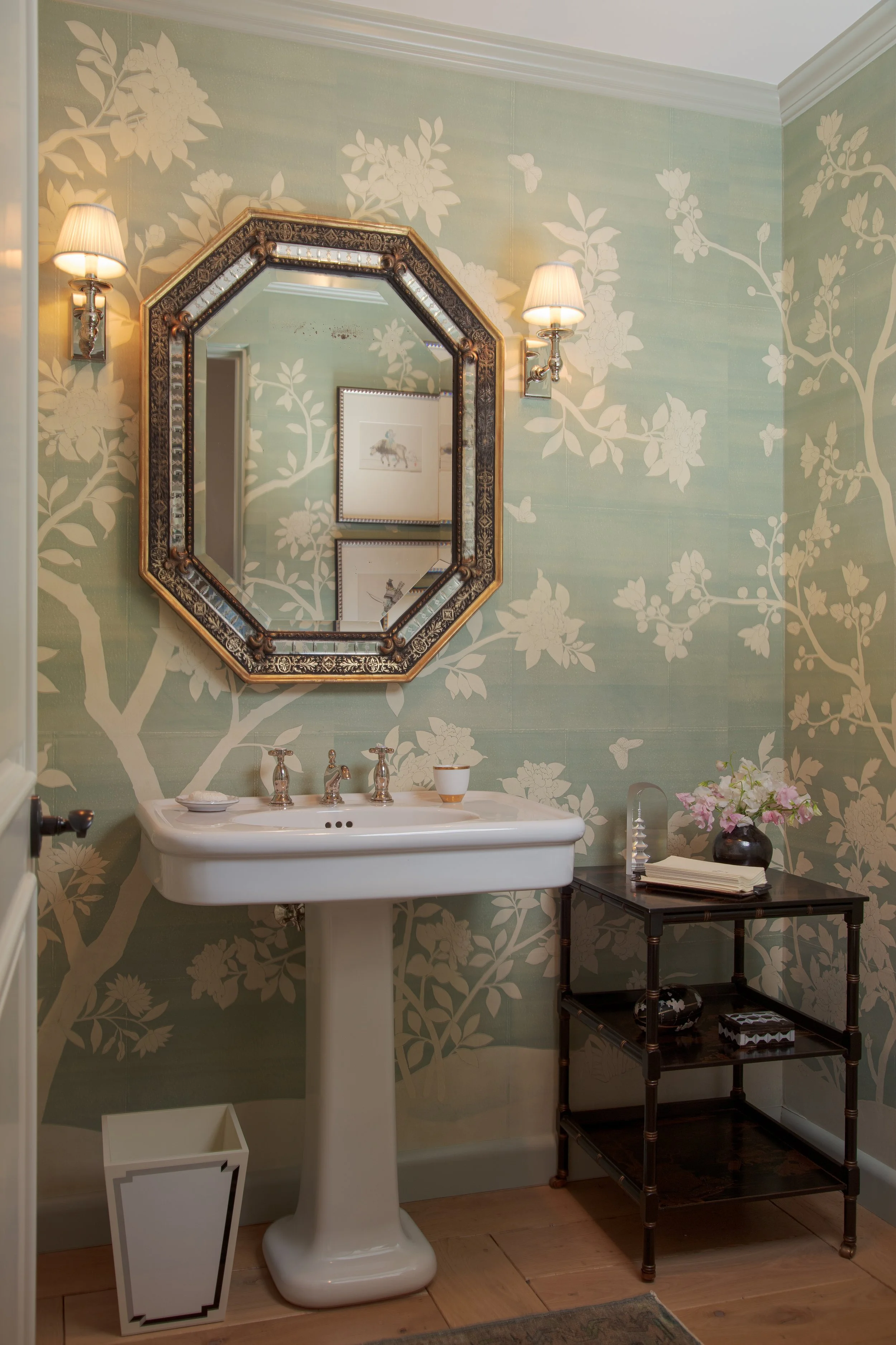 Powder room with a pedestal sink, an octagonal mirror and green wallpaper with a pale branch and blossom pattern