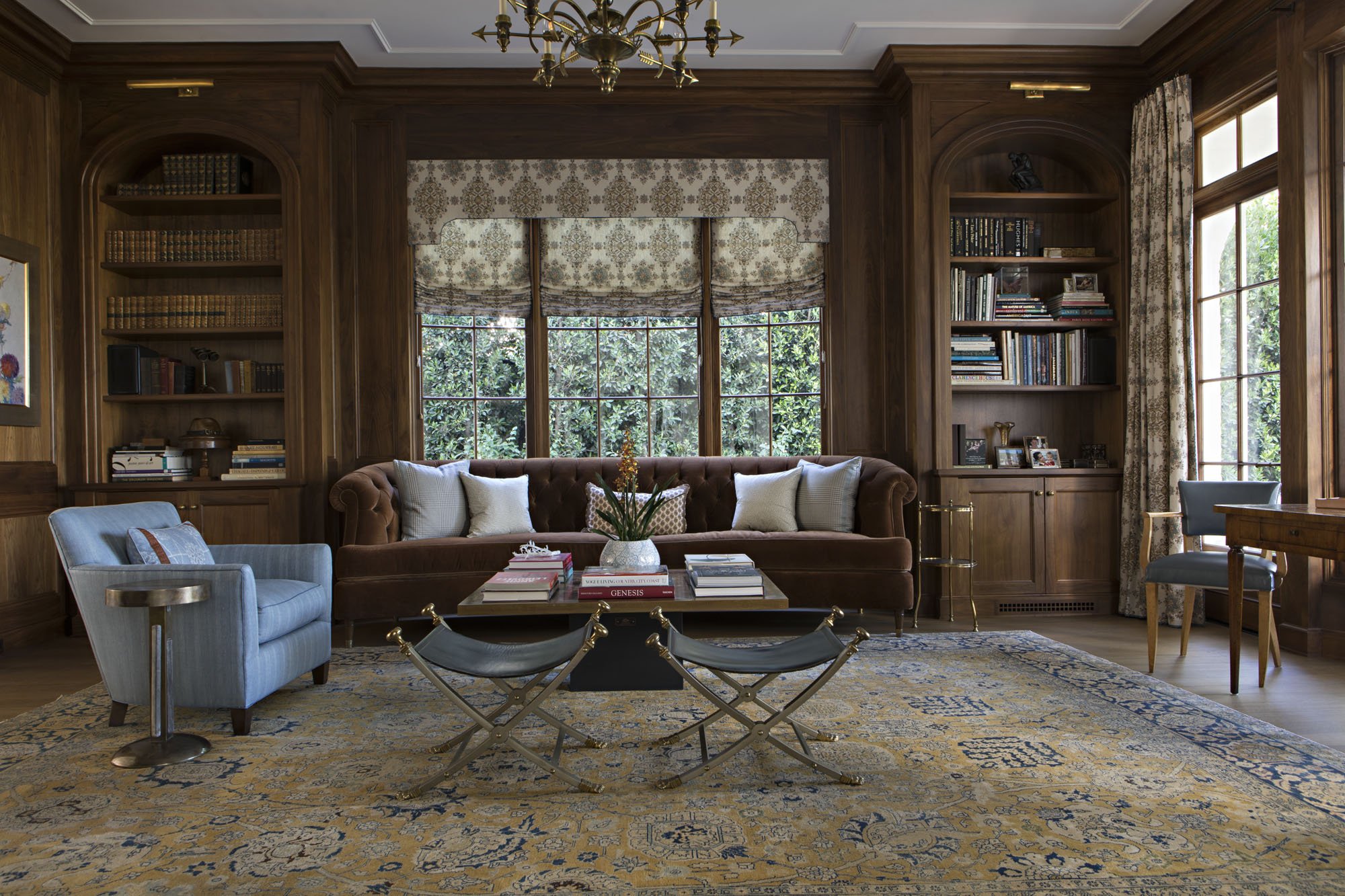 Paneled library with built-in bookshelves, brown velvet sofa and patterned roman shades