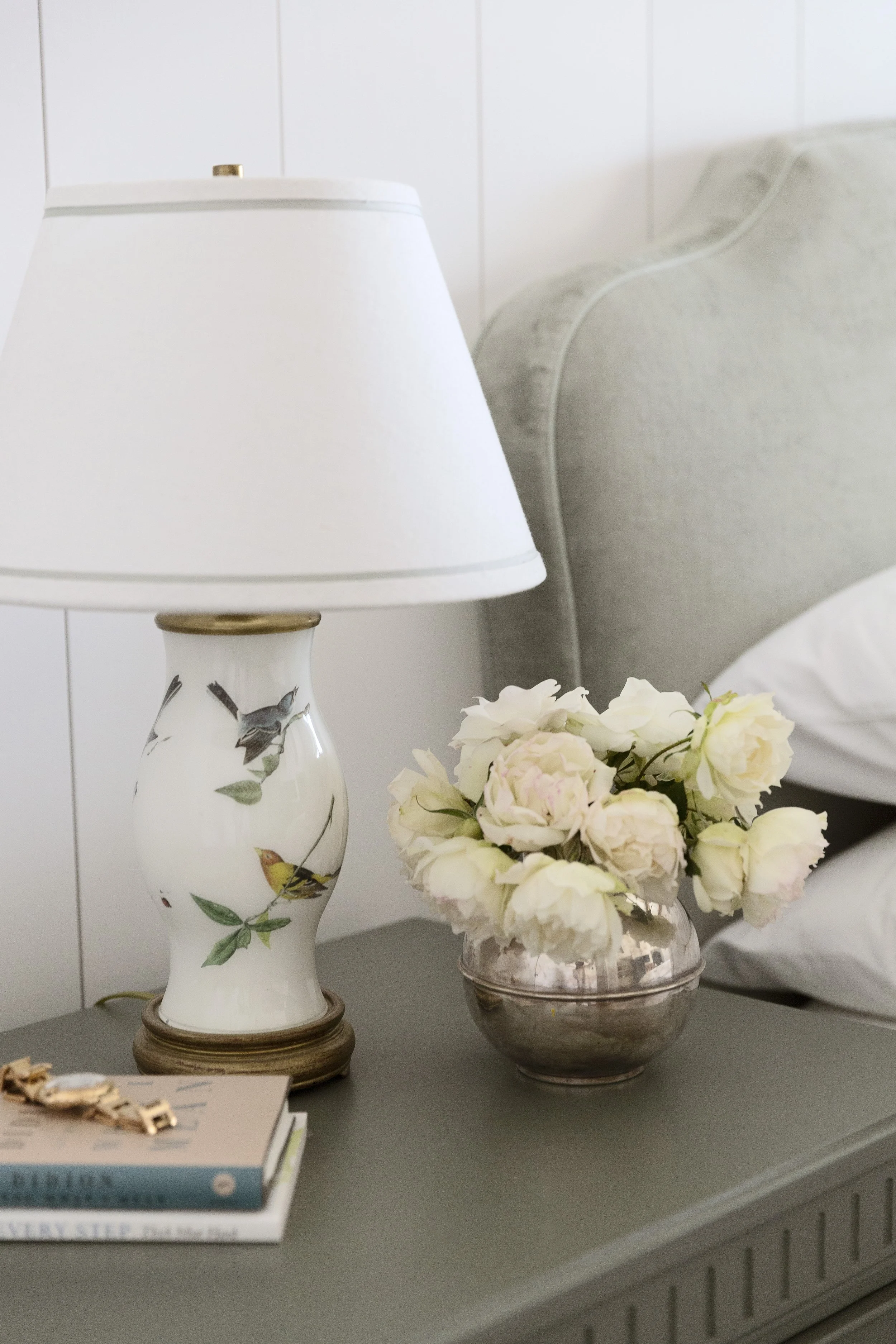 Bedside lamp with a painted bird motif beside white roses