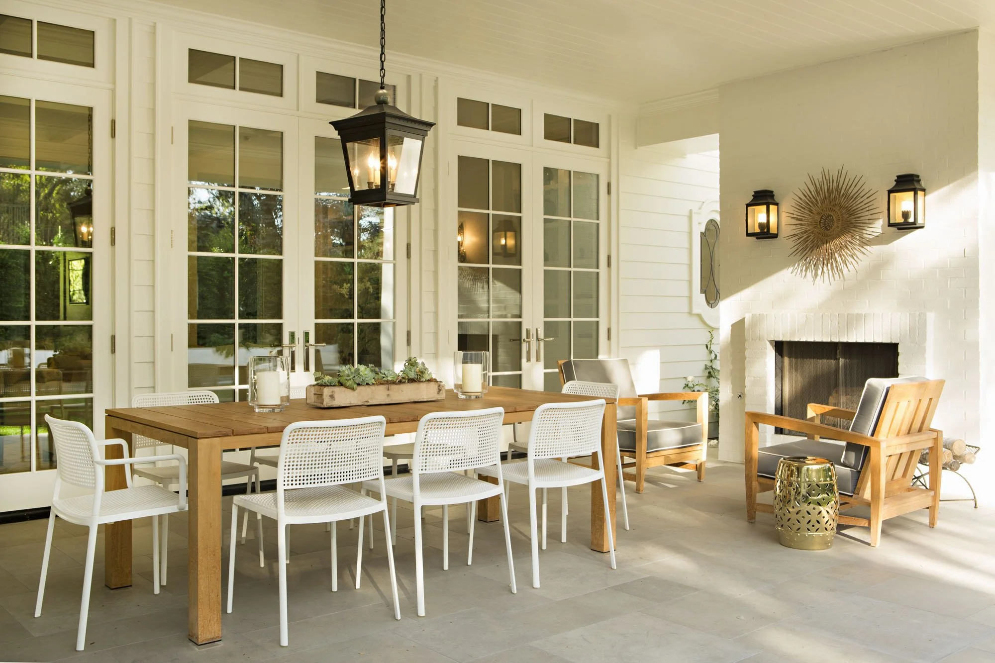 Sunroom dining area with a wood table, white chairs, French doors and a black lantern