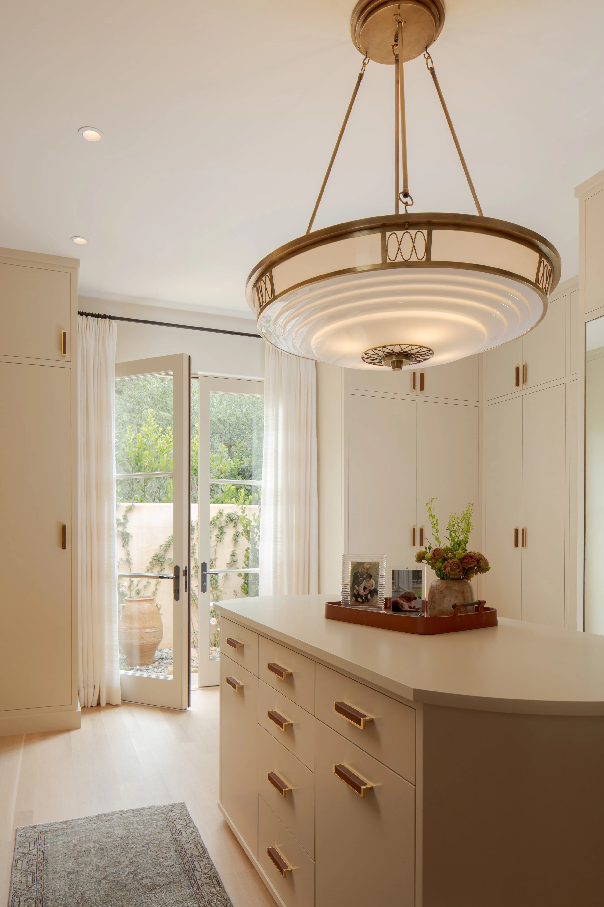 Dressing room with built-in cabinetry, a scalloped ring pendant light, a center island and French doors to a terrace