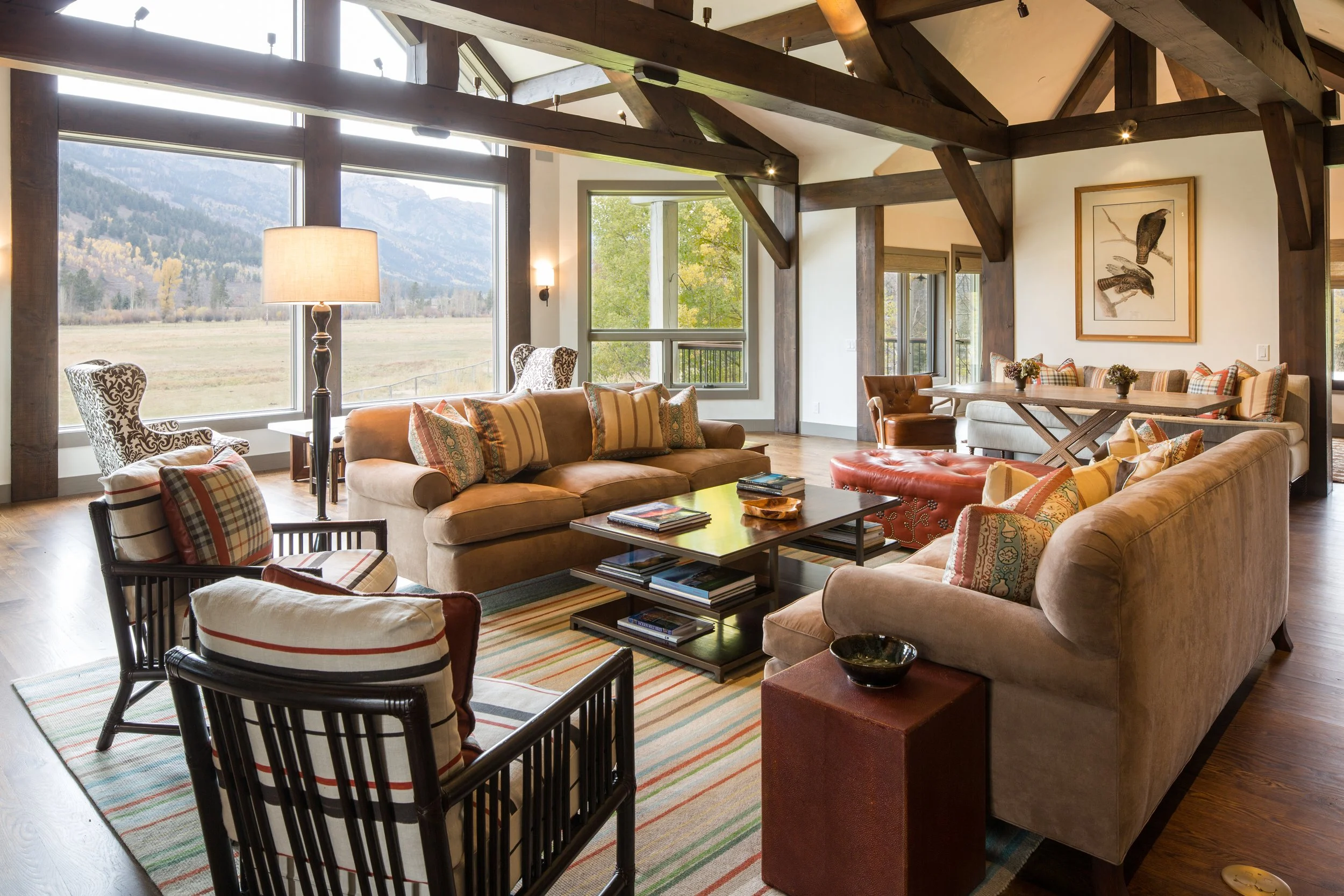 Great room with timber trusses, a tan sofa, striped pillows and mountain views through tall windows