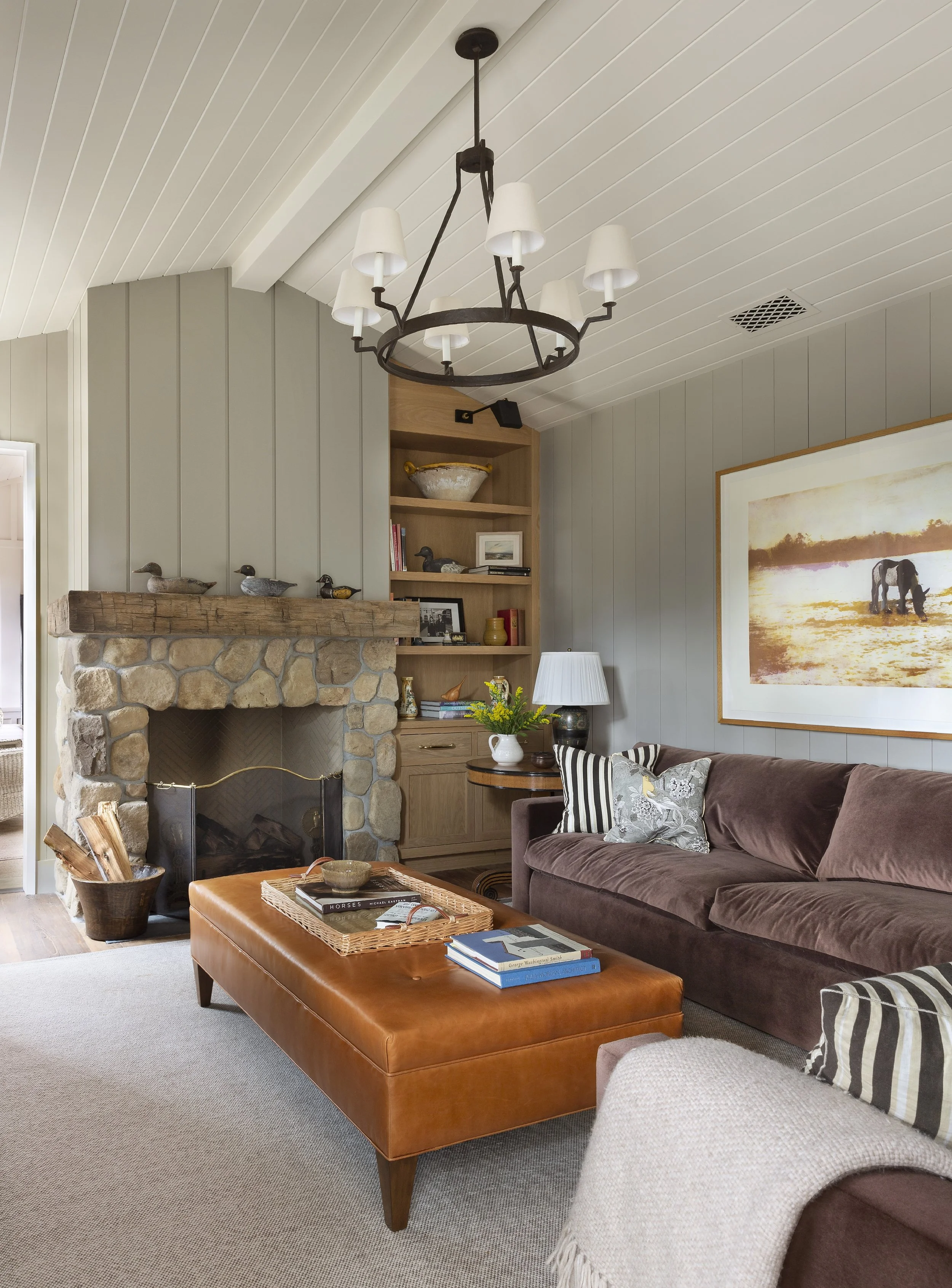Family room with a stone fireplace, built-in shelves, plum velvet sofa and framed landscape art