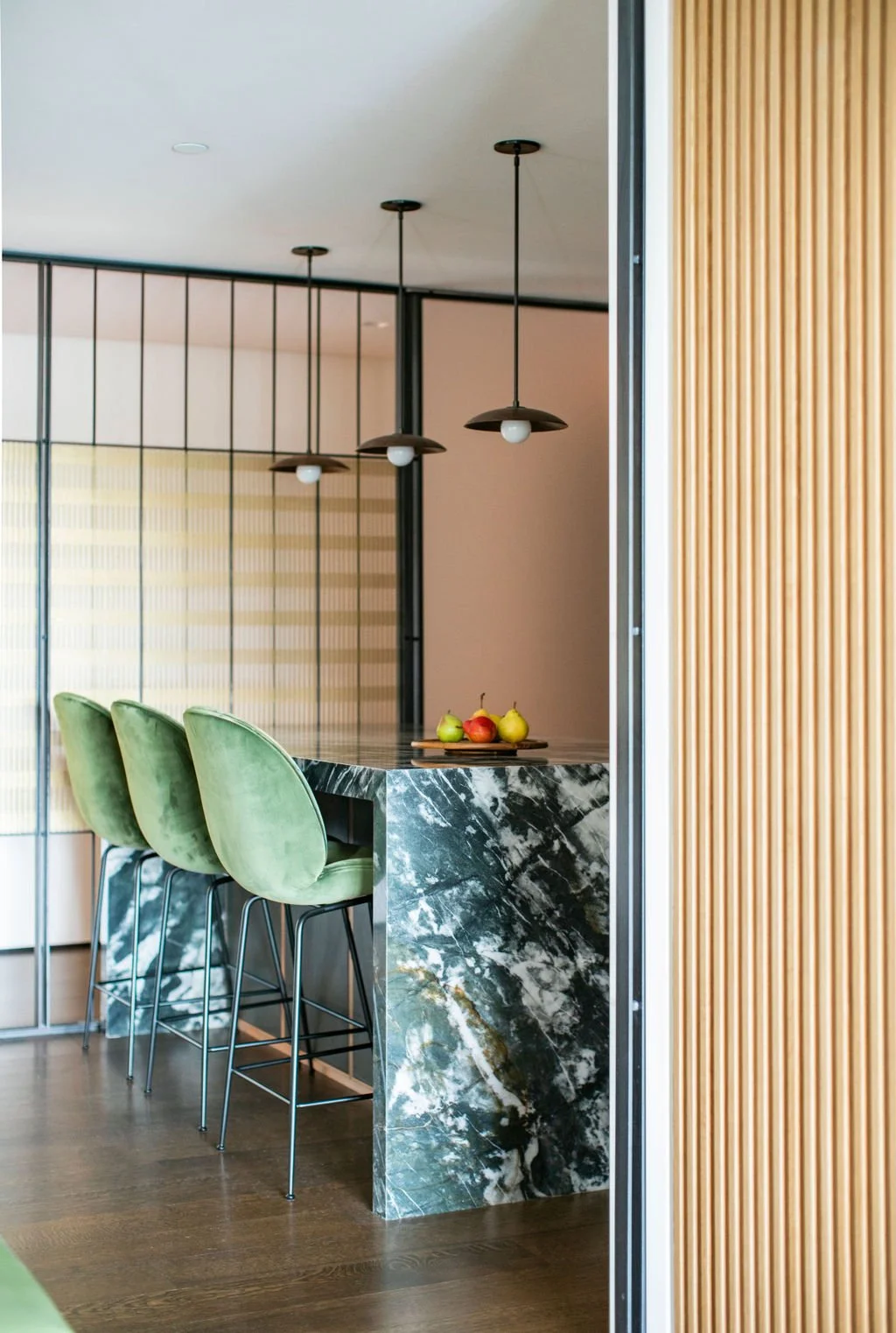 Green velvet counter stools at a dark green stone island with slatted white oak behind