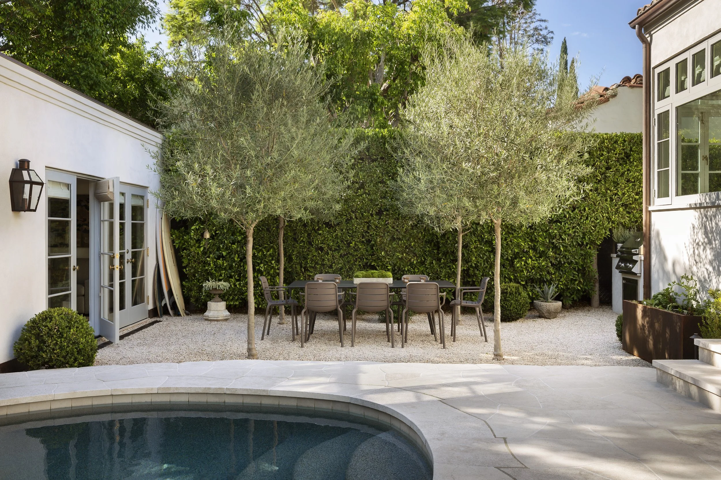 Patio with olive trees and a dining table beside the pool