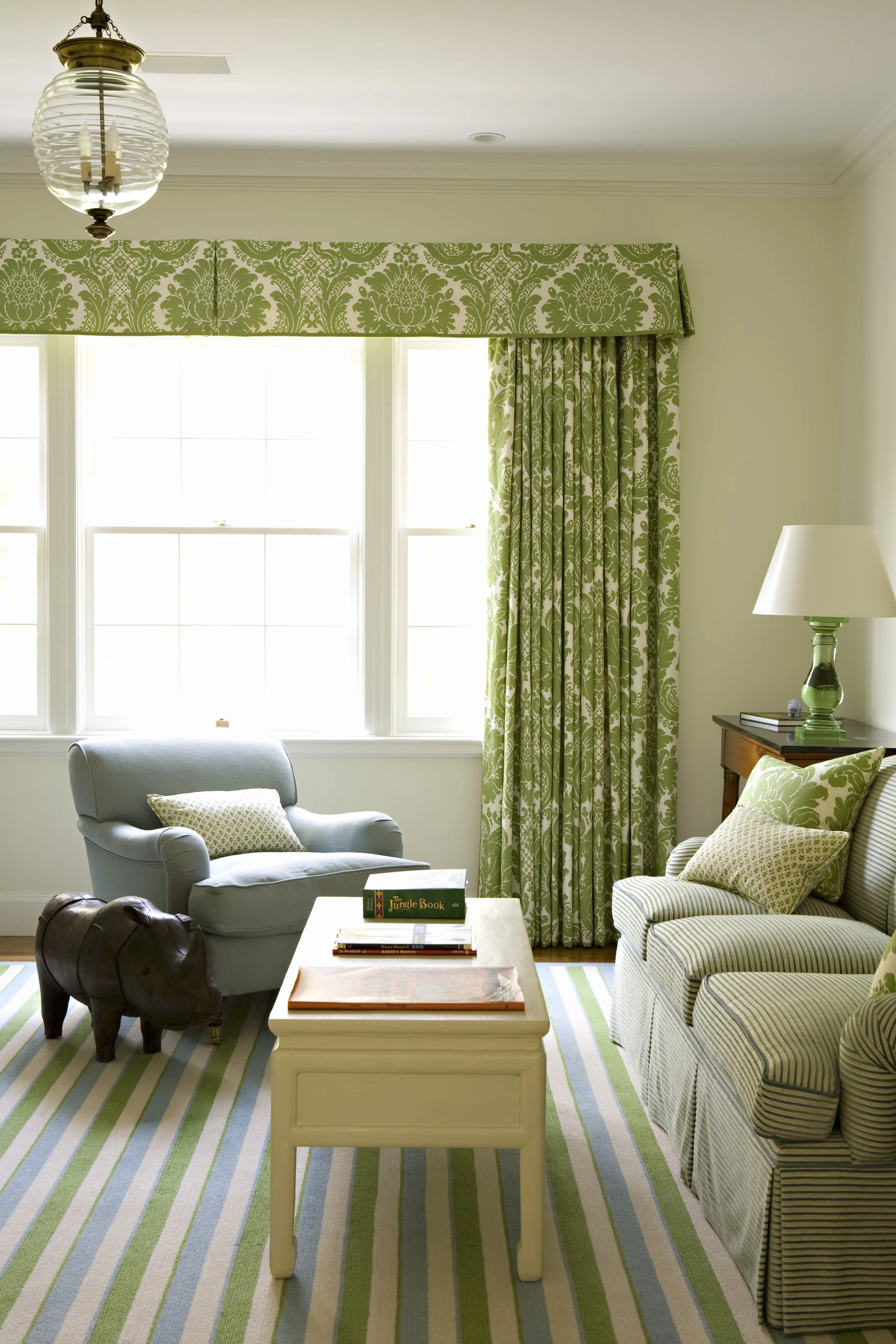 Sitting area with a blue armchair, green floral curtains and a table lamp
