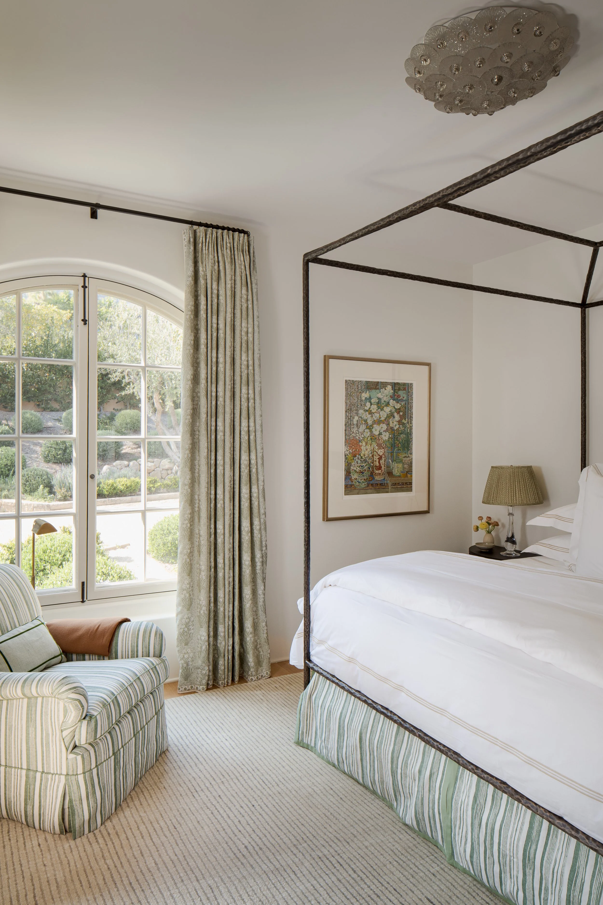 Bedroom with a black canopy bed, an arched window, long green curtains and a framed botanical print
