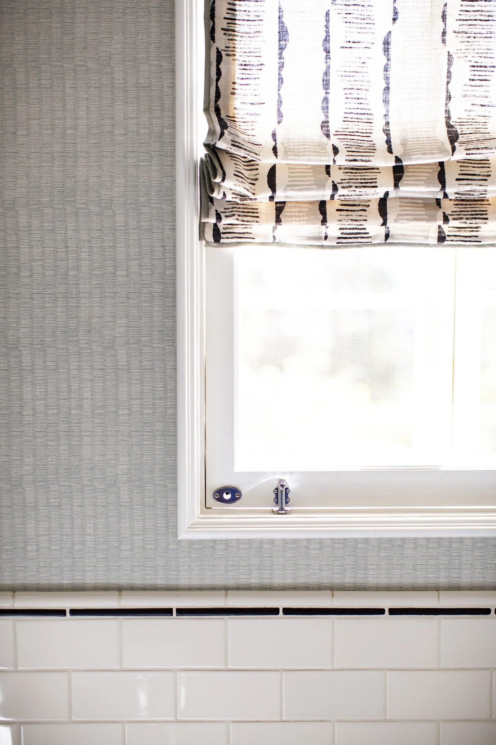 Guest bath window with a black-and-cream block-print Roman shade, a gray textured wallcovering and white subway tile