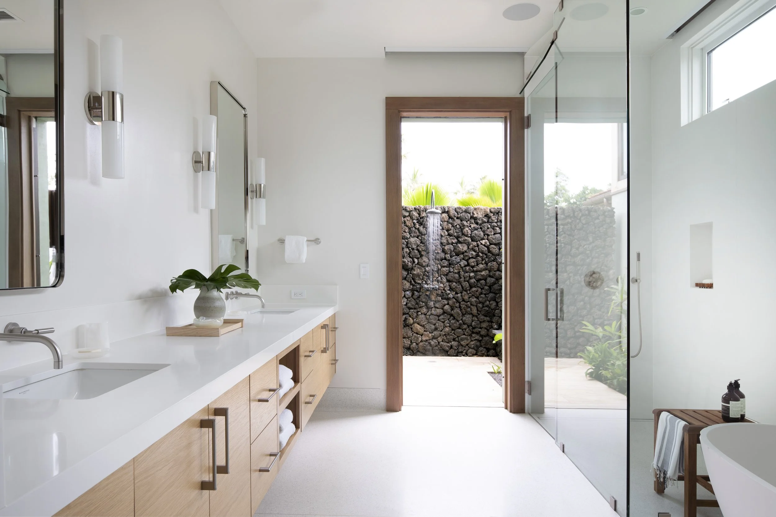 Primary bath with an oak vanity, glass shower and a lava rock outdoor shower beyond