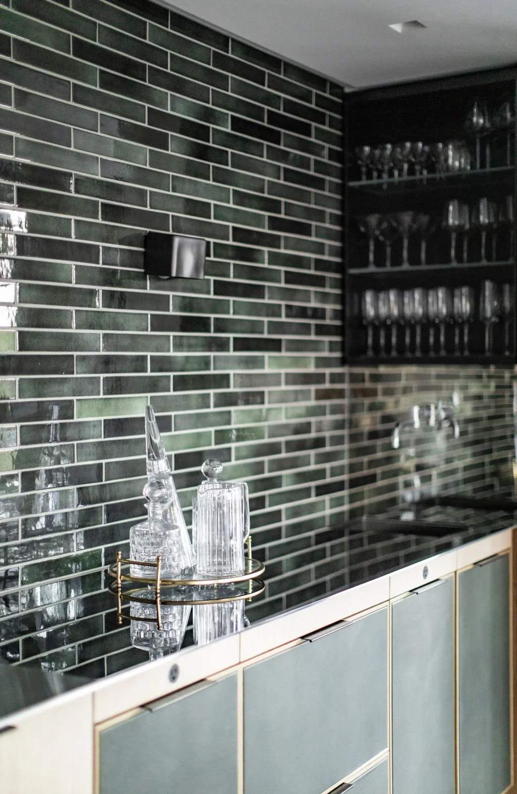 Wet bar with green handmade tile, glass shelving and a brass bar cart