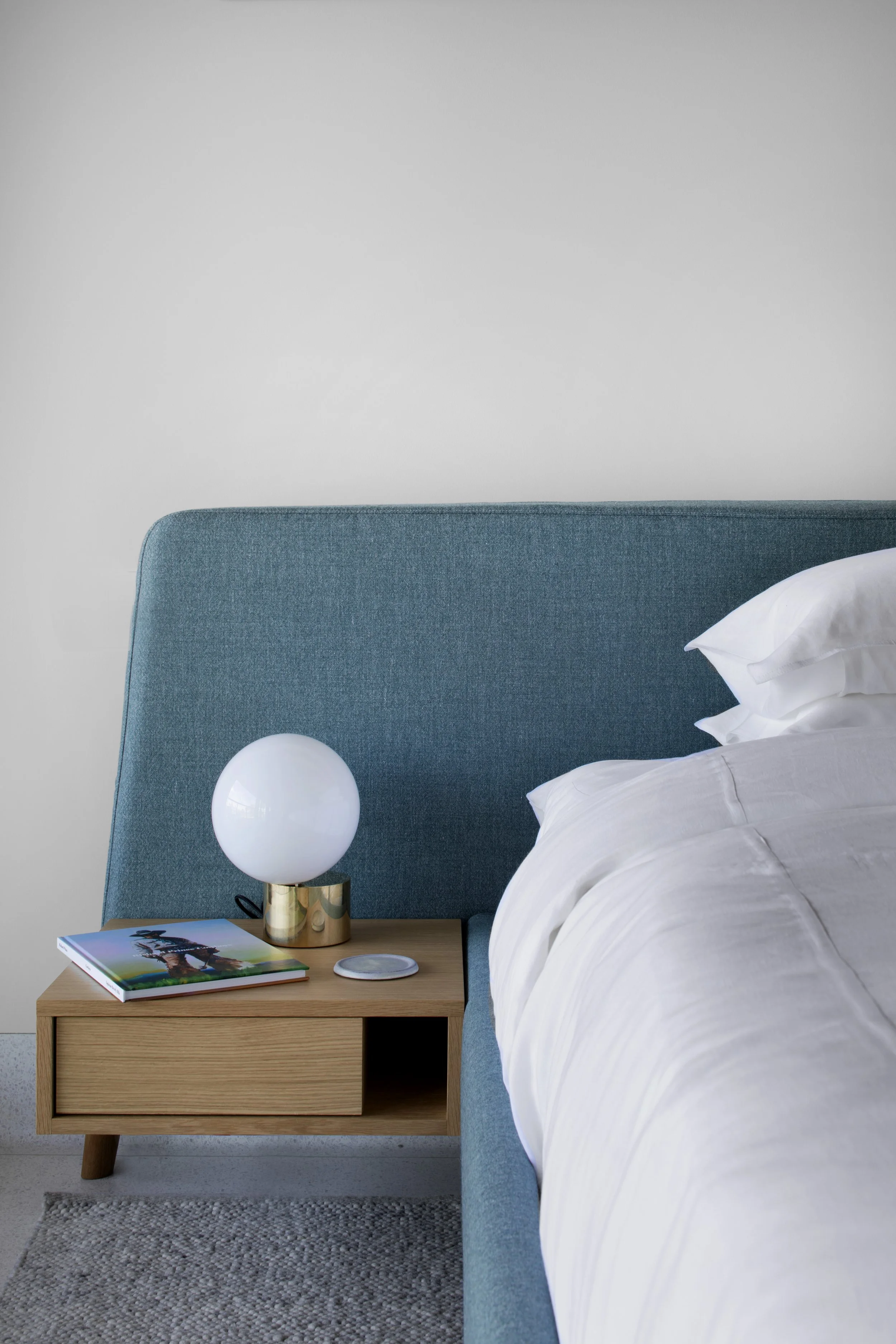 Bedside detail with a teal upholstered headboard and a globe lamp
