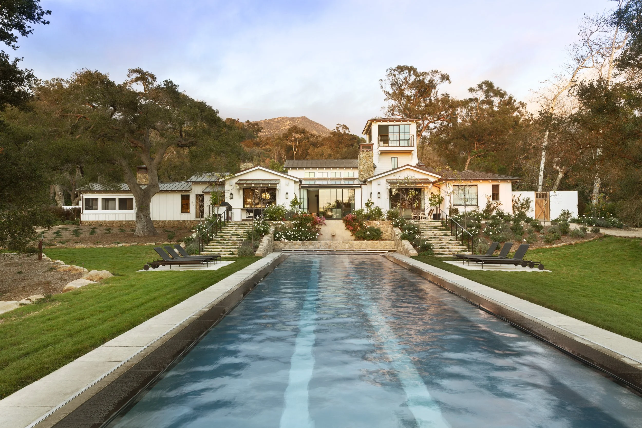 Long reflecting pool and lawn leading to the white farmhouse among oaks