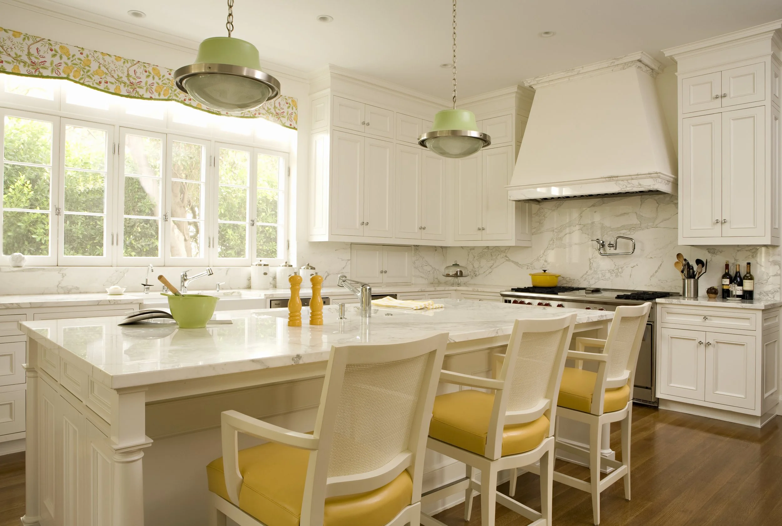 White kitchen with an island, yellow counter stools and green pendant lights