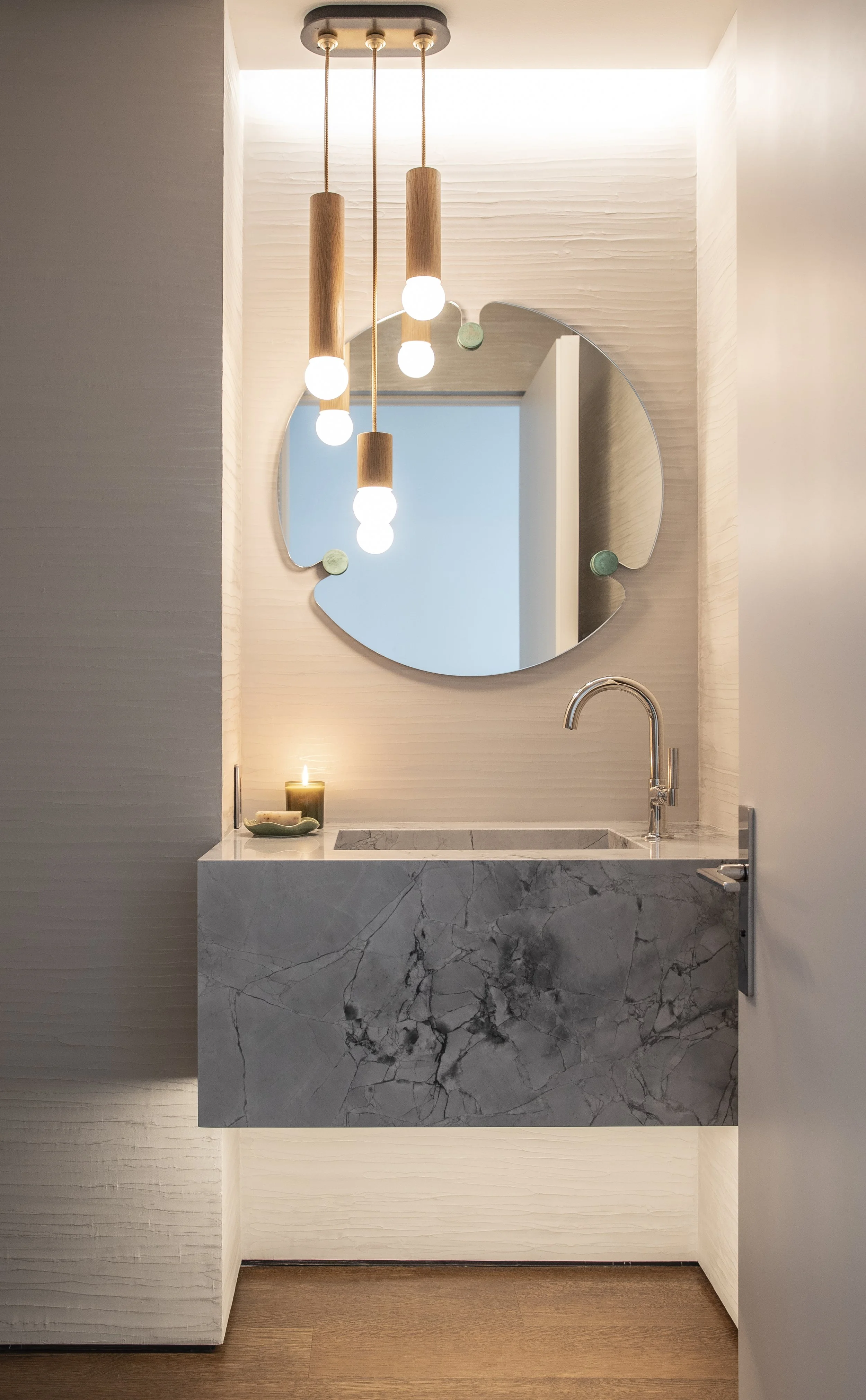 Powder room with a round mirror, floating stone sink and warm pendant lights