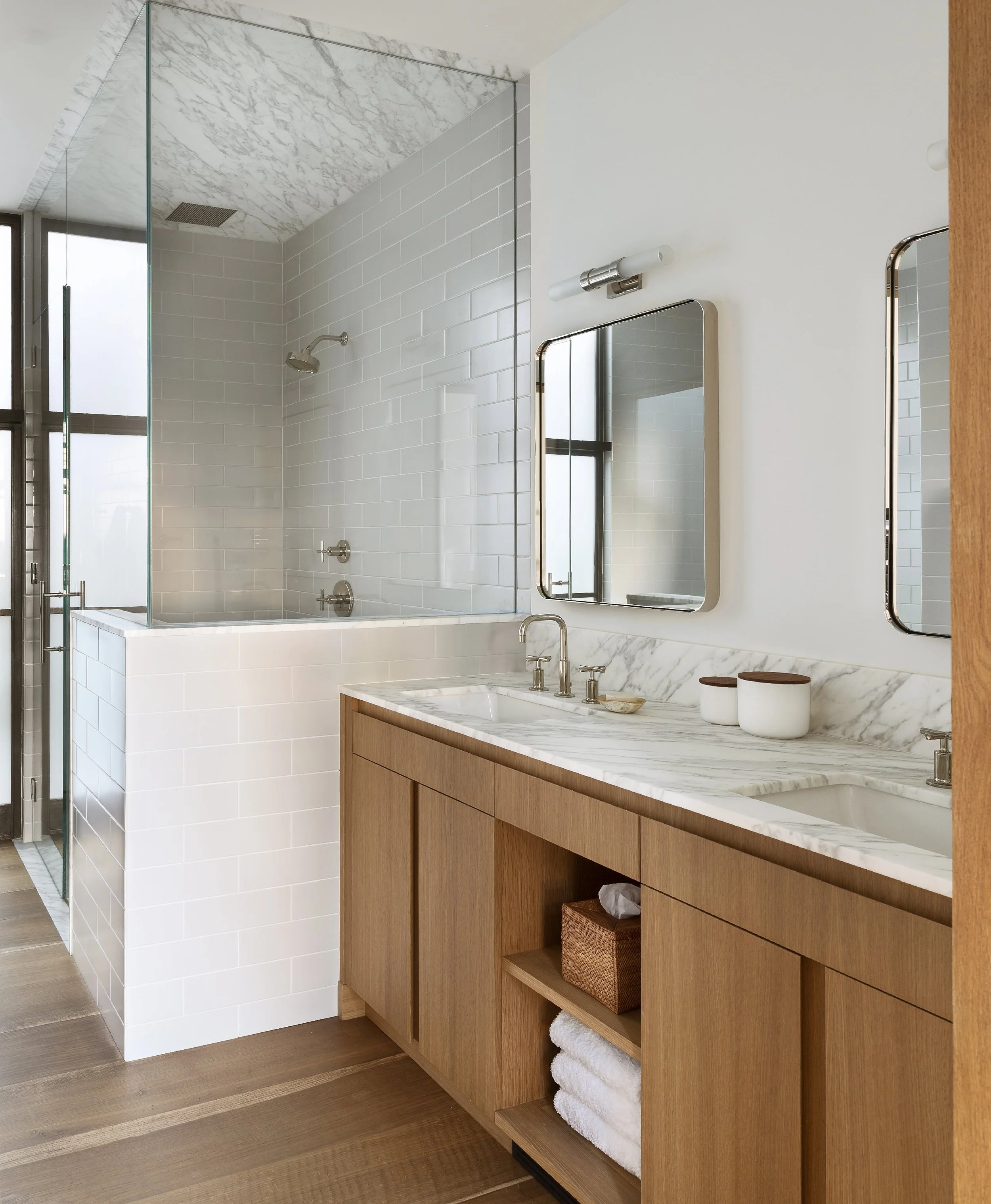 Bath with an oak double vanity, marble counter and a tiled shower