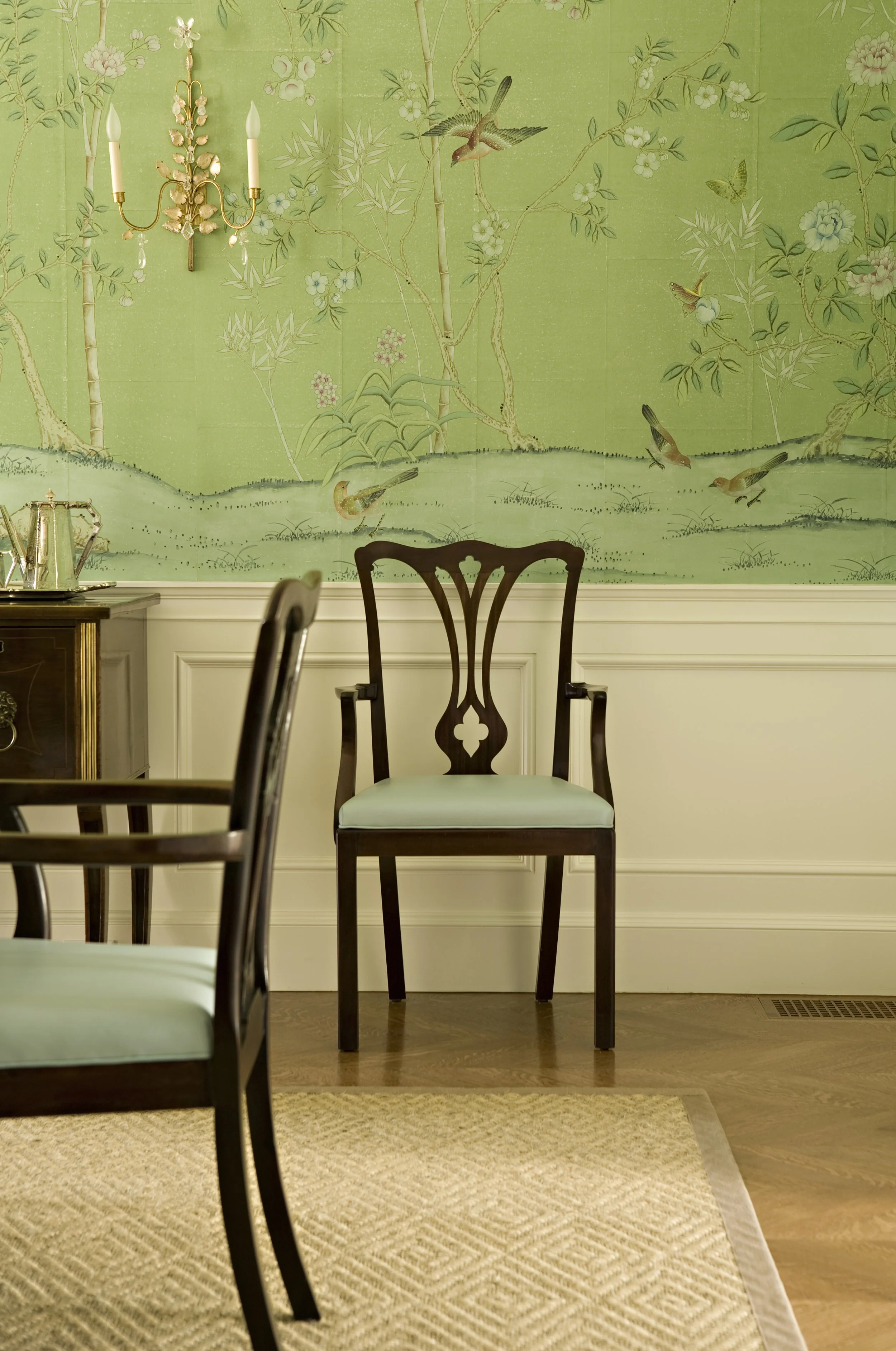 Dining chair with a pale green seat against hand painted green wallpaper and white wainscot