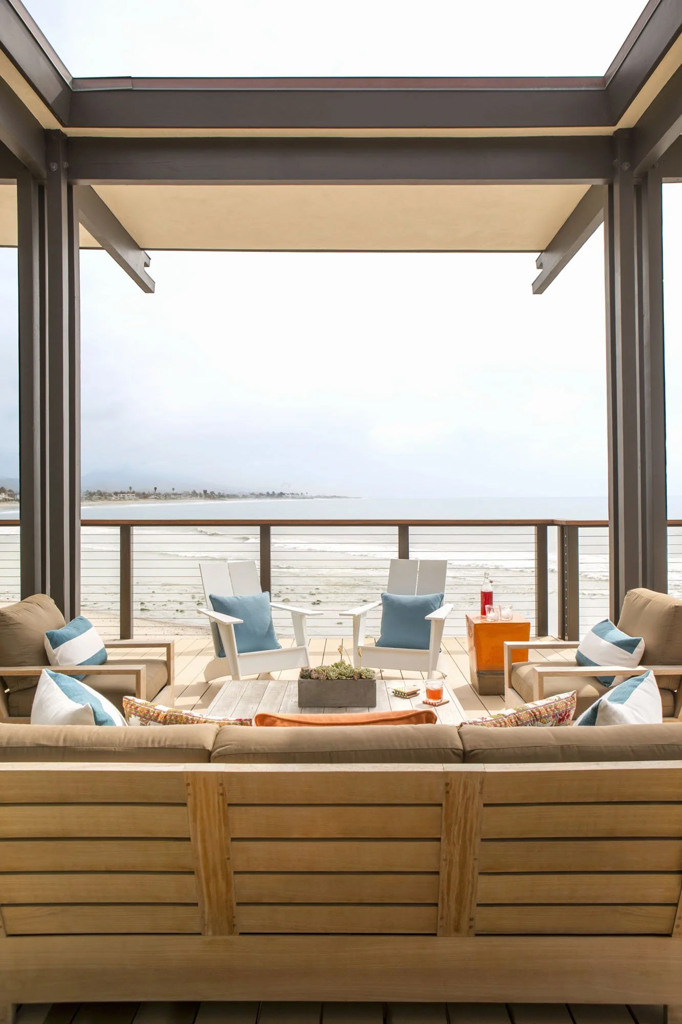 Covered deck with a sofa, white Adirondack chairs and blue pillows overlooking the beach