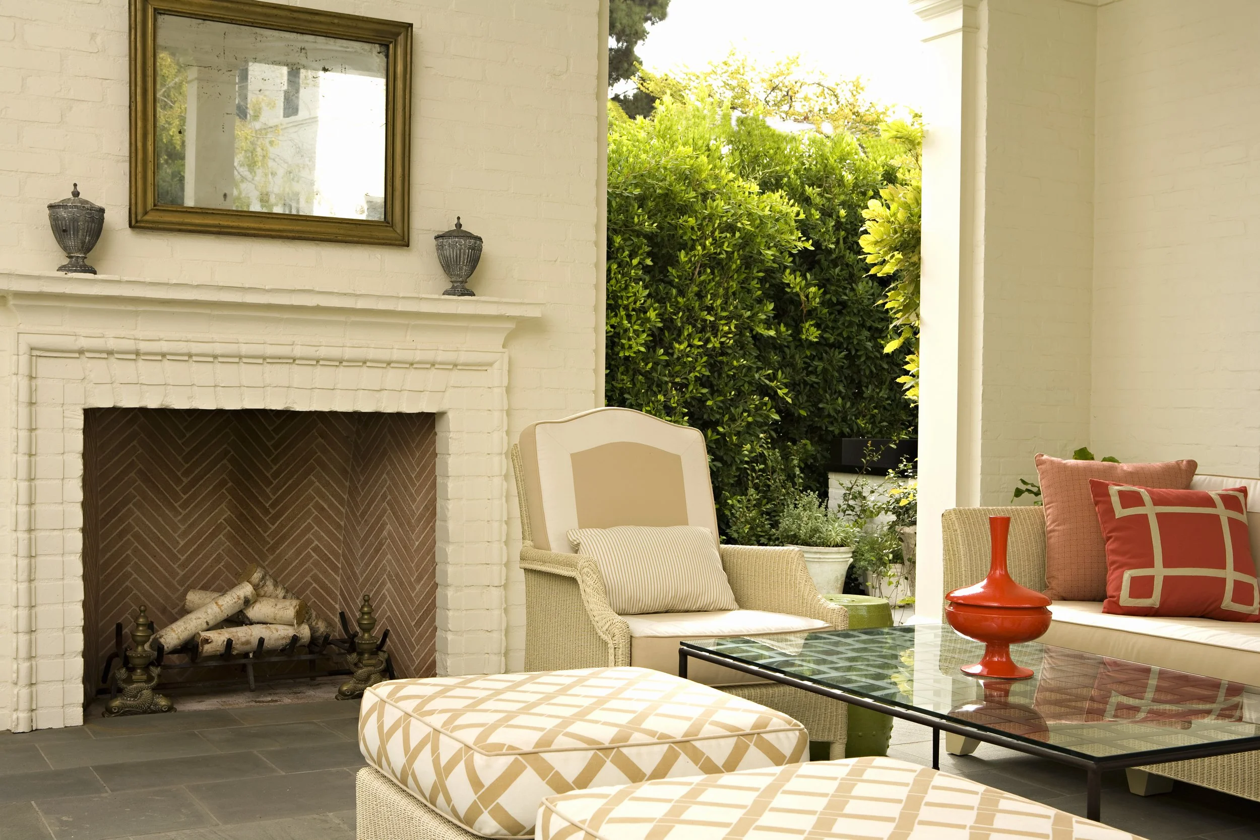 Covered outdoor living room with a brick fireplace, cream lounge chairs and coral pillows