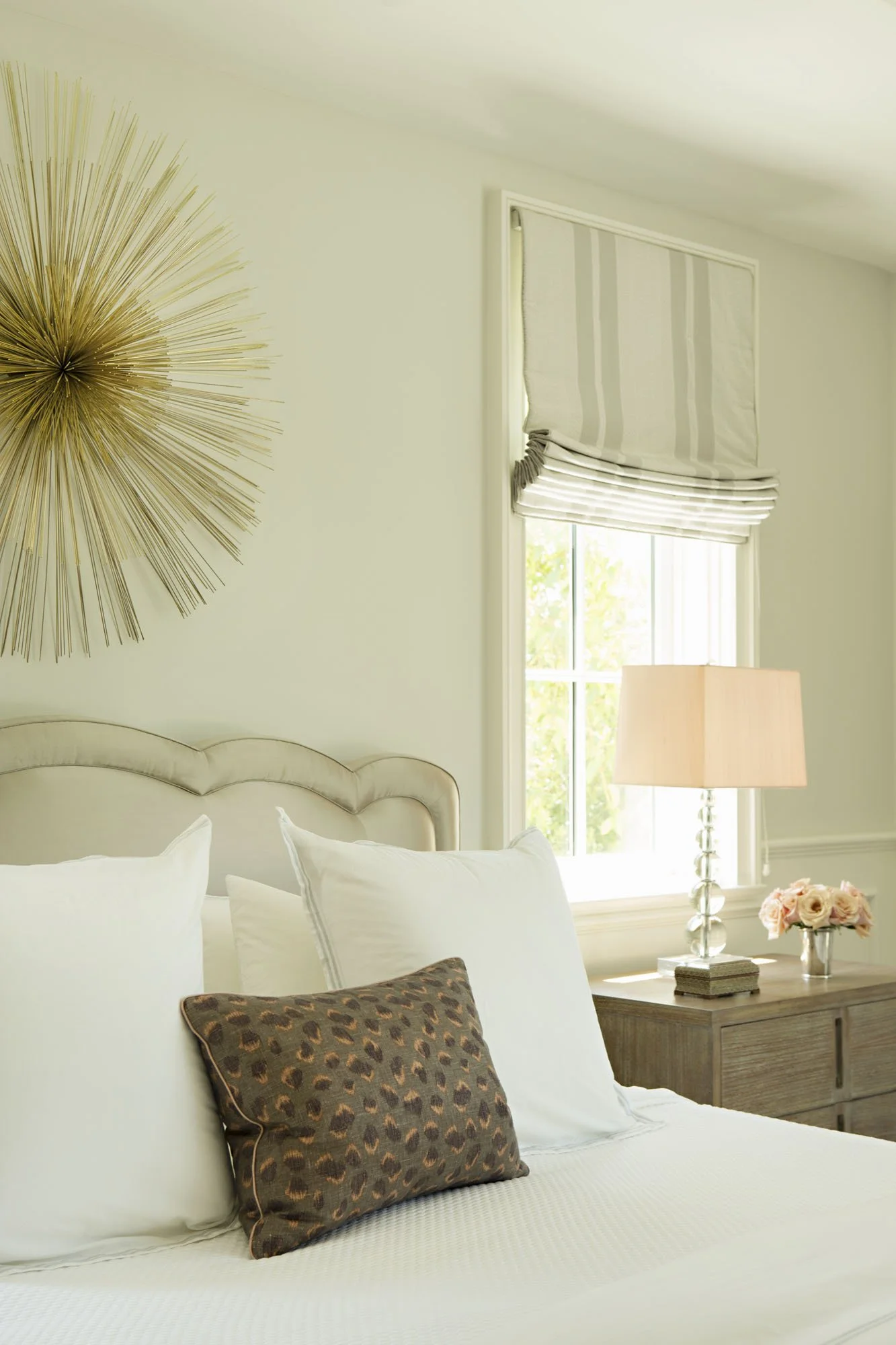 Bedside detail with a gilded sunburst, crystal lamp and soft roman shade