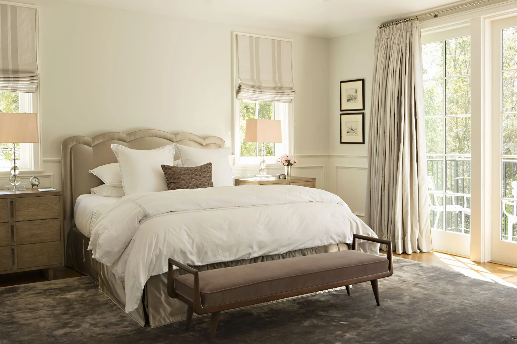 Primary bedroom with an upholstered scalloped headboard, tailored bench and wainscoted walls