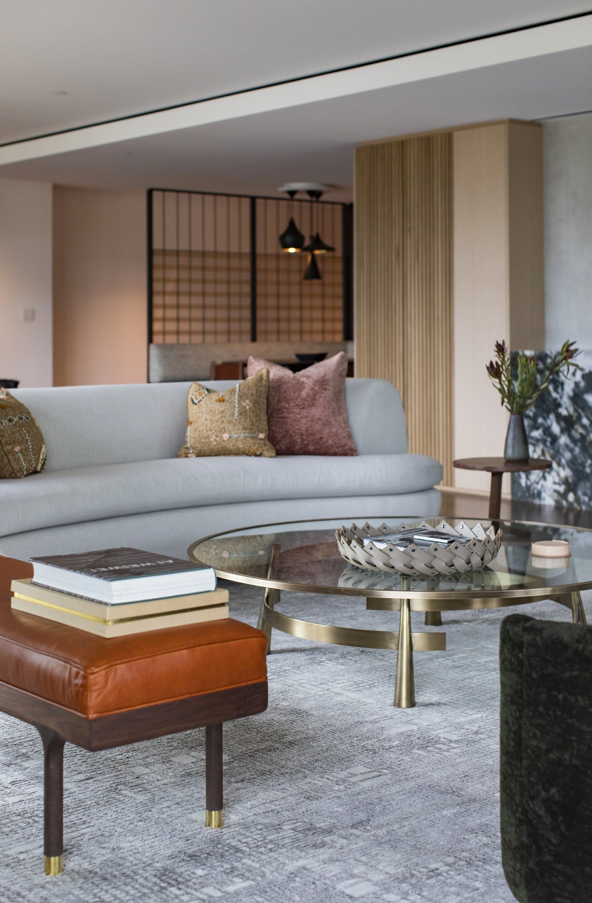 Living room with a curved gray sofa, brass and glass coffee table and slatted wood screens