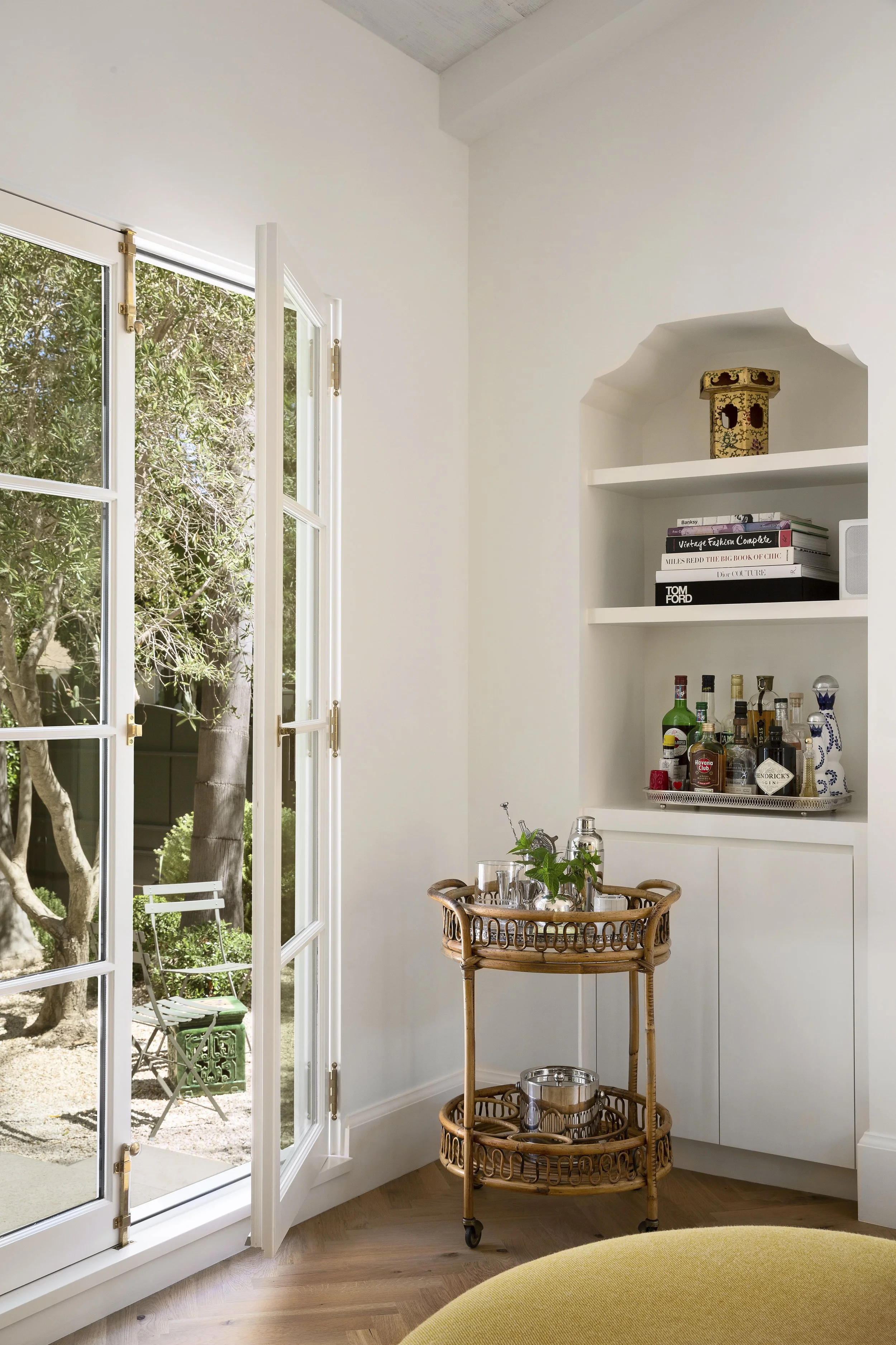 French doors to olive trees beside a built-in bar niche with a rattan cart