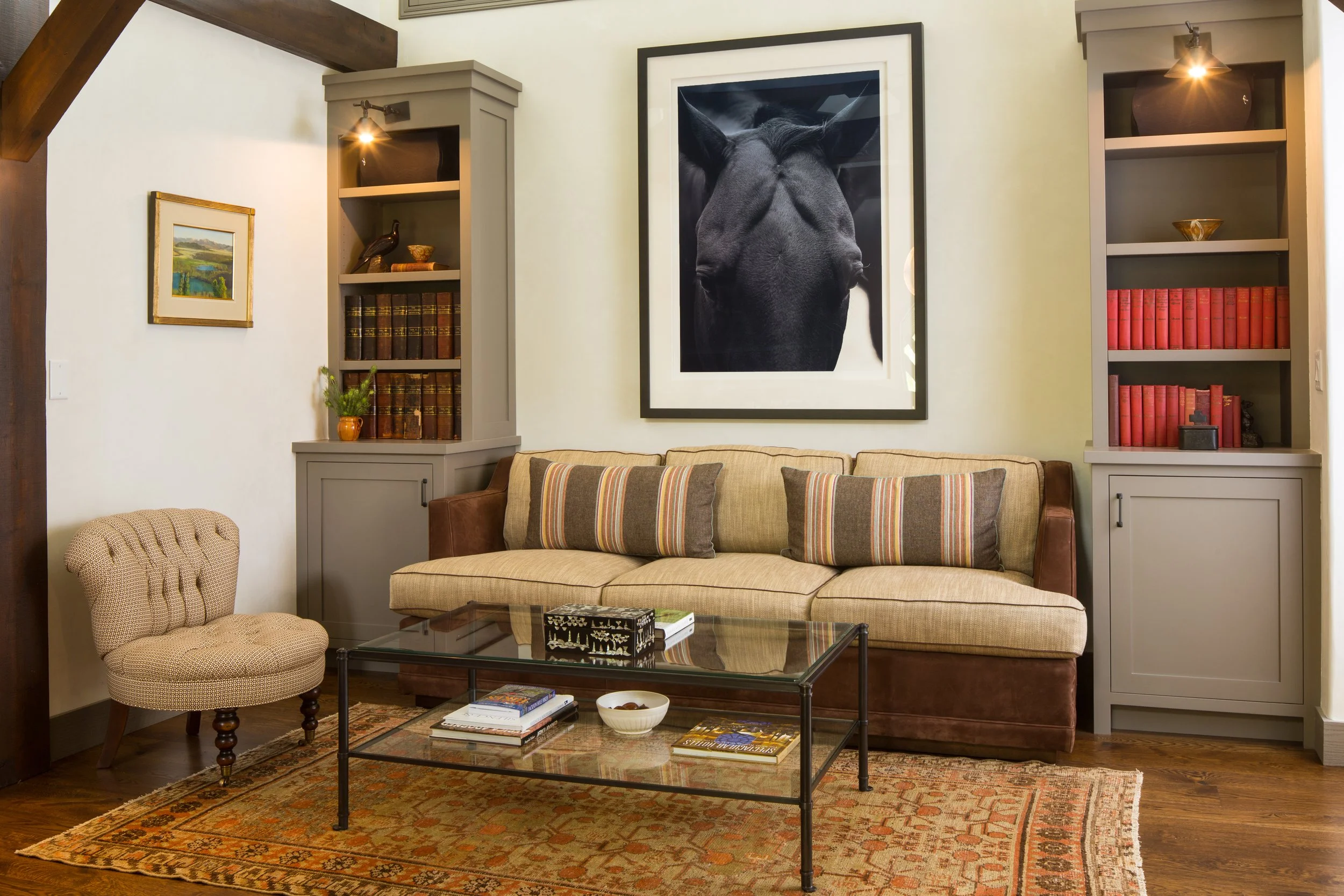 Sitting room with a striped sofa, a glass coffee table, built-in bookshelves, a framed black and white photograph and an antique rug