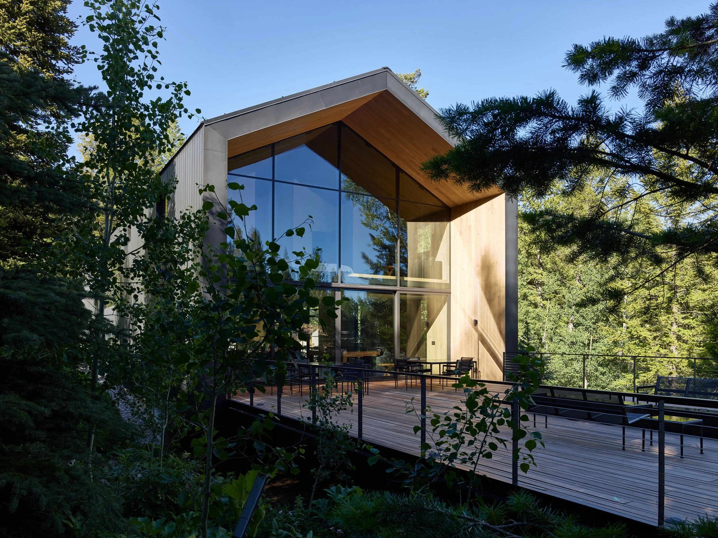 Gabled glass facade among aspen and pine trees with a steel railed deck