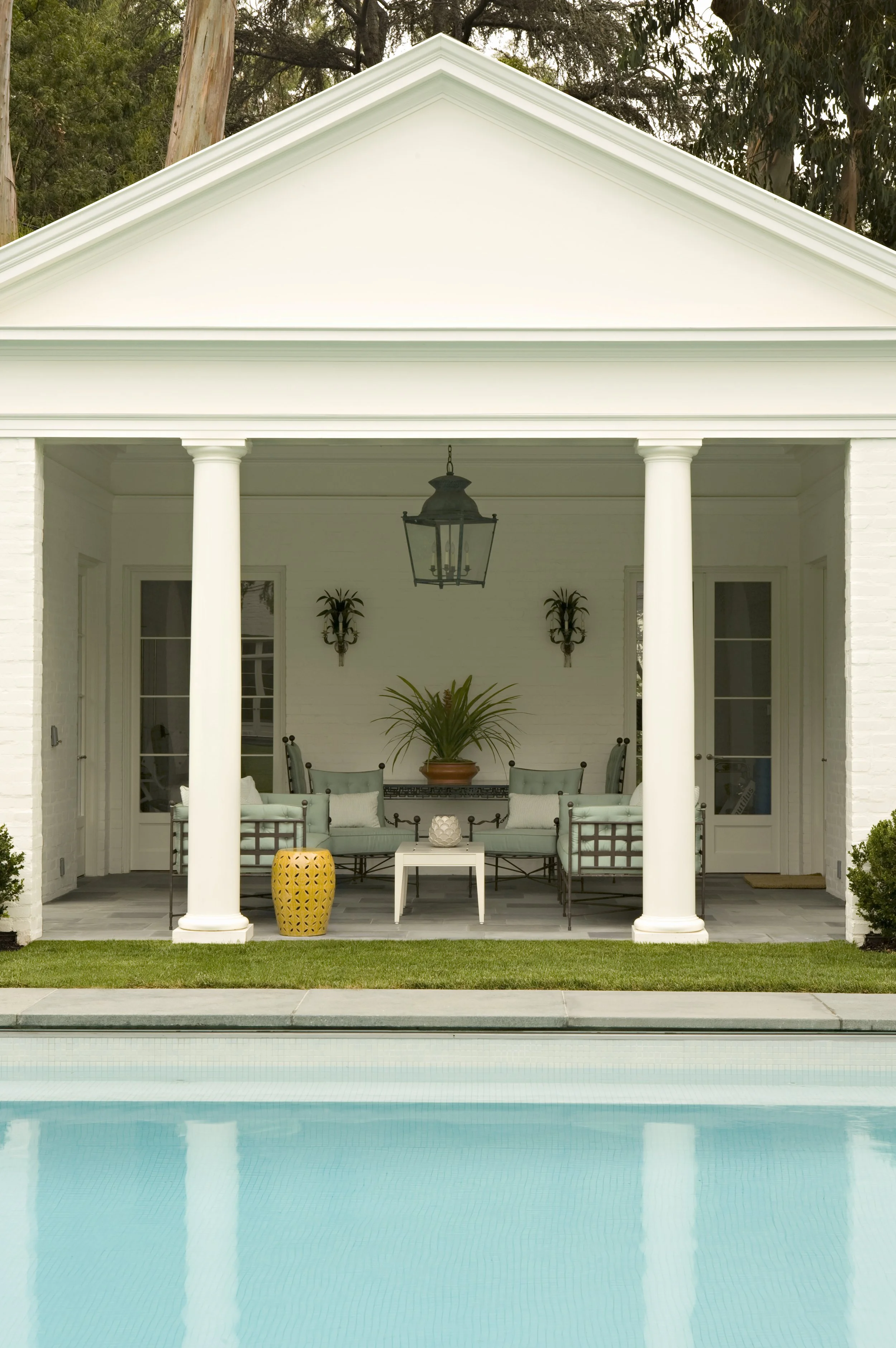 Covered porch with white columns, a lantern, dining table and teal chairs