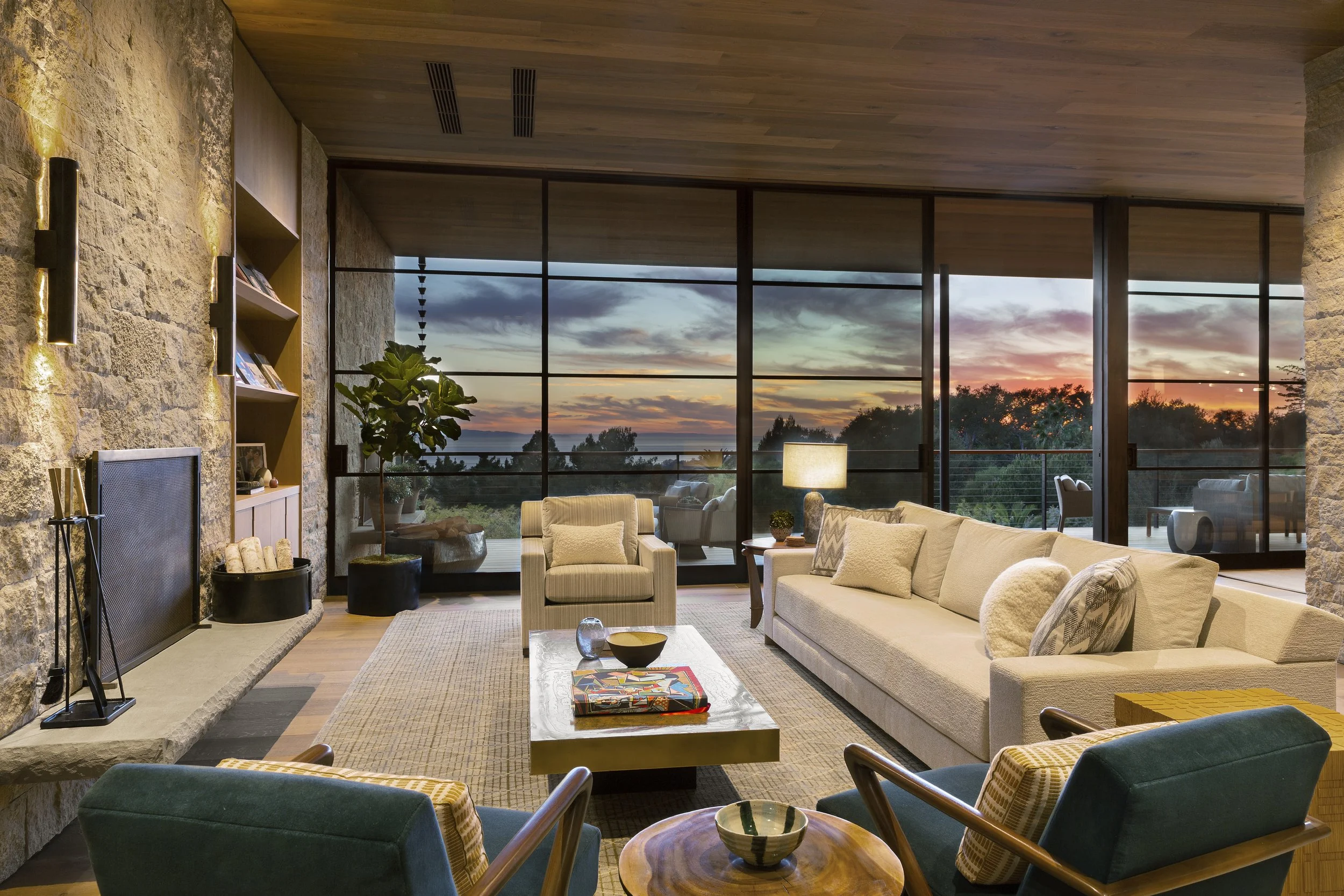 Living room at dusk with a wood ceiling, glass walls and sunset views