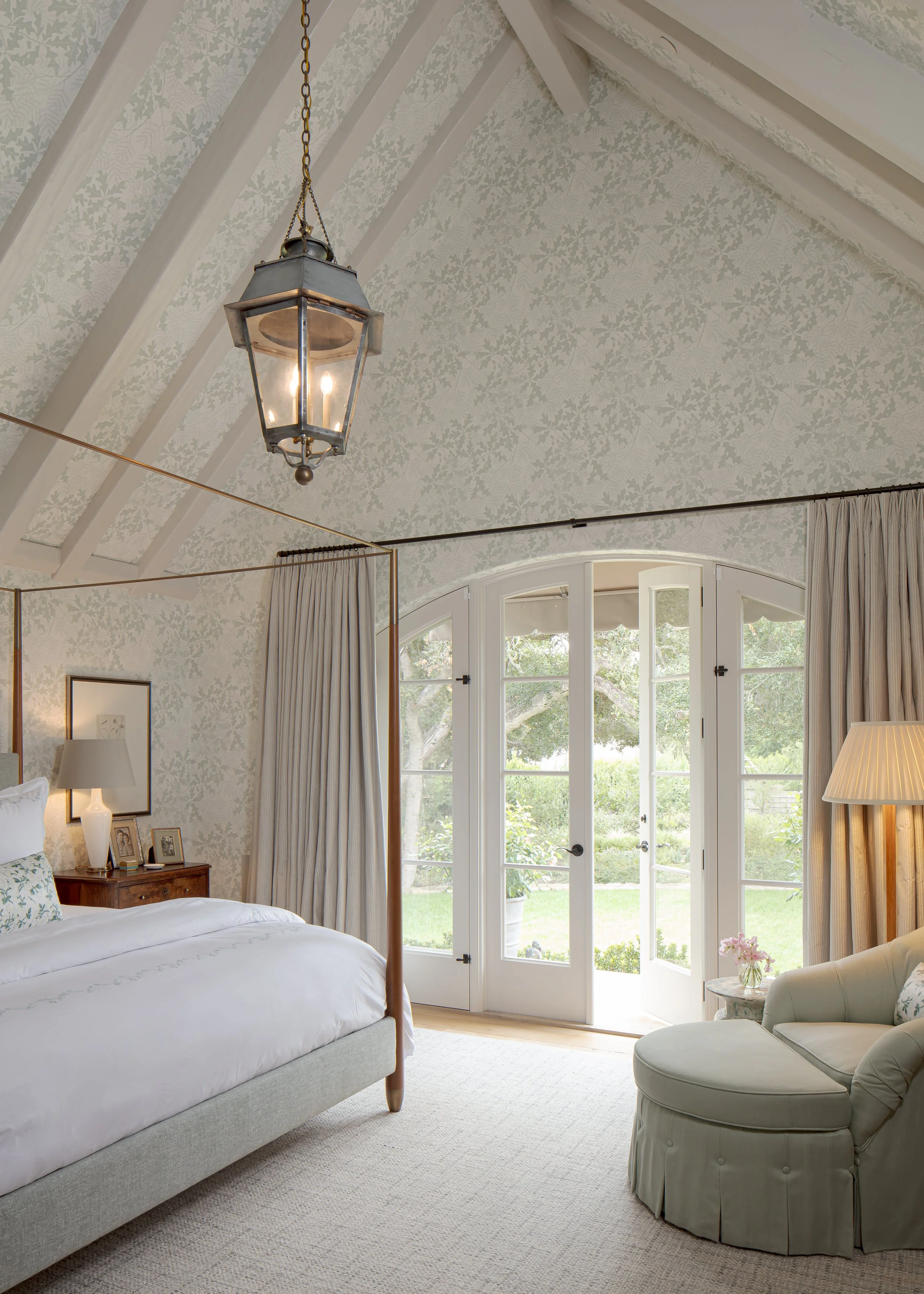 Bedroom with a pitched ceiling, a glass lantern, arched French doors to the garden and soft gray floral wallpaper